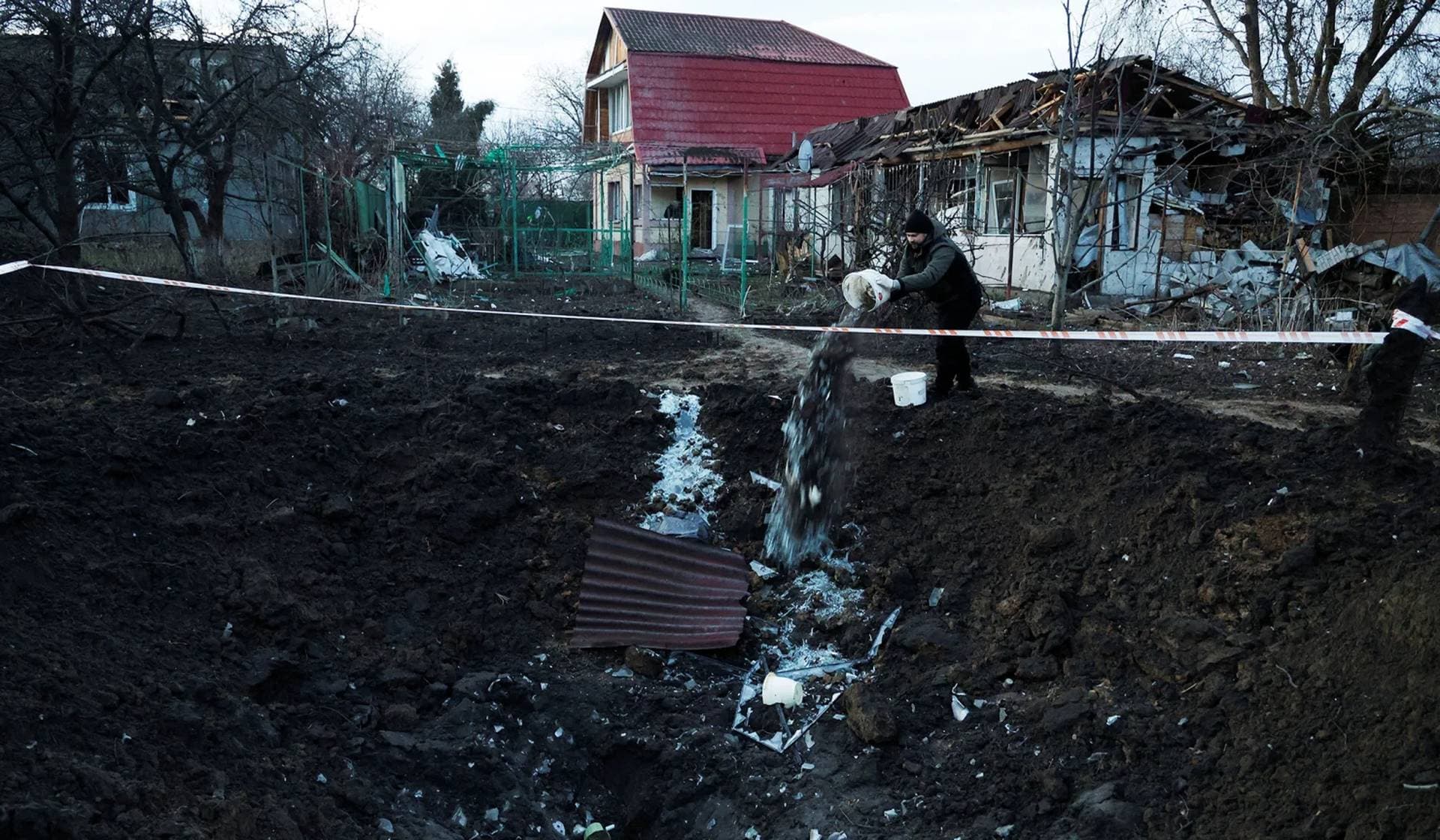A man drops debris into a crater in his backyard after a Russian missile strike in Kyiv