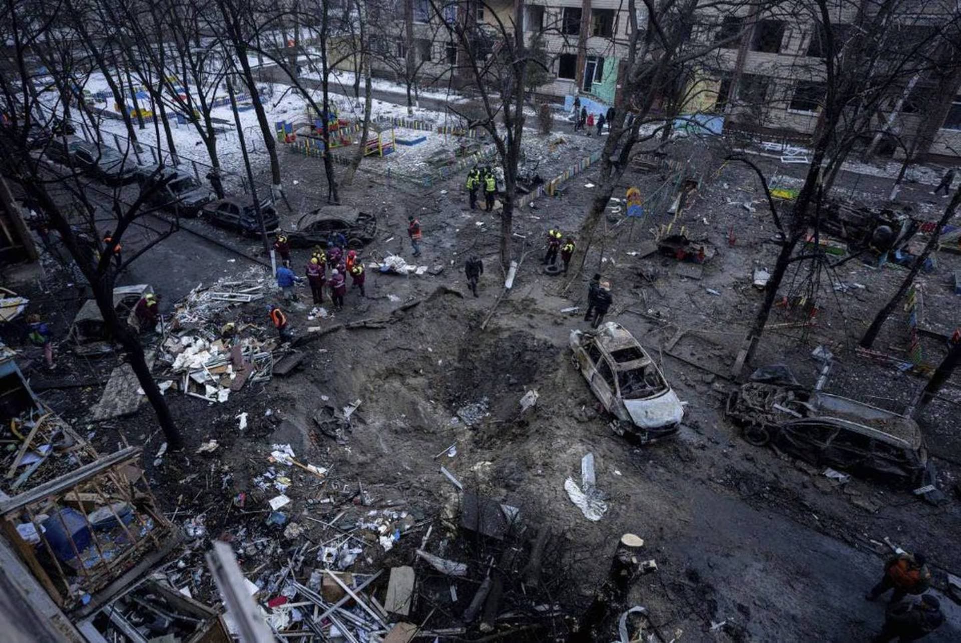 People stand near a crater in the yard of a damaged multi-store building after a Russian attack at residential neighbourhood in Kyiv
