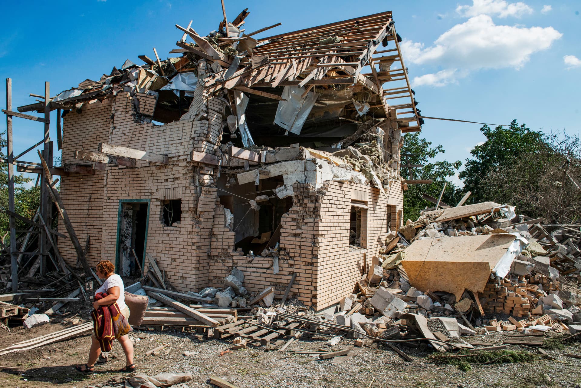 A local resident carries belongings from the ruins of her house destroyed in a Russian missile strike in Kyiv region