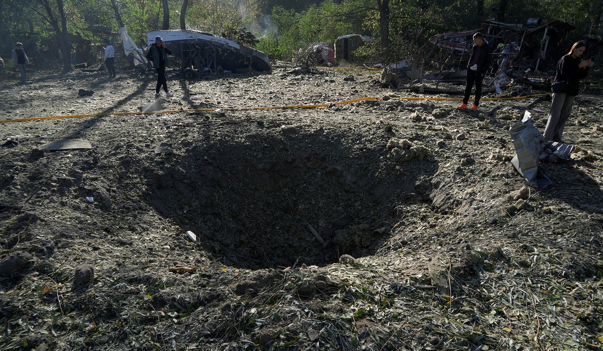 Residents stand next to a crater that appeared at the site of an open-air restaurant after a Russian missile strike in Kyiv
