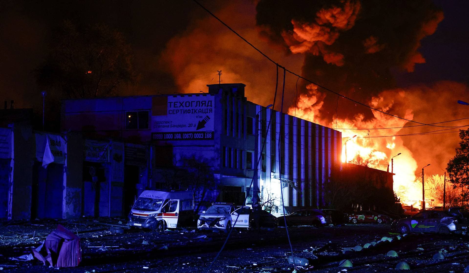 A police officer stands next to a police car and an ambulance vehicle which were damaged during a Russian missile strike in Kyiv