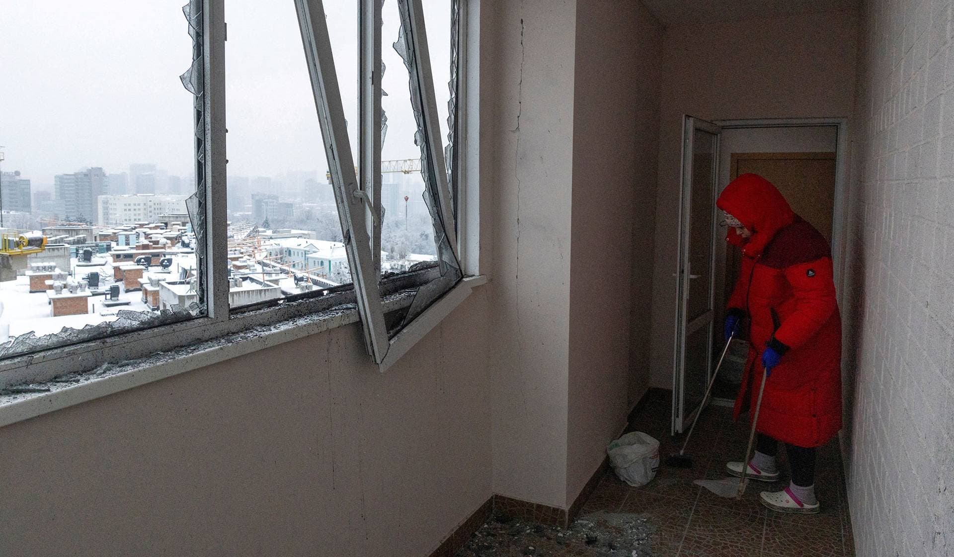 A resident cleans broken glass from a corridor after a Russian drone hit her apartment building in Kyiv