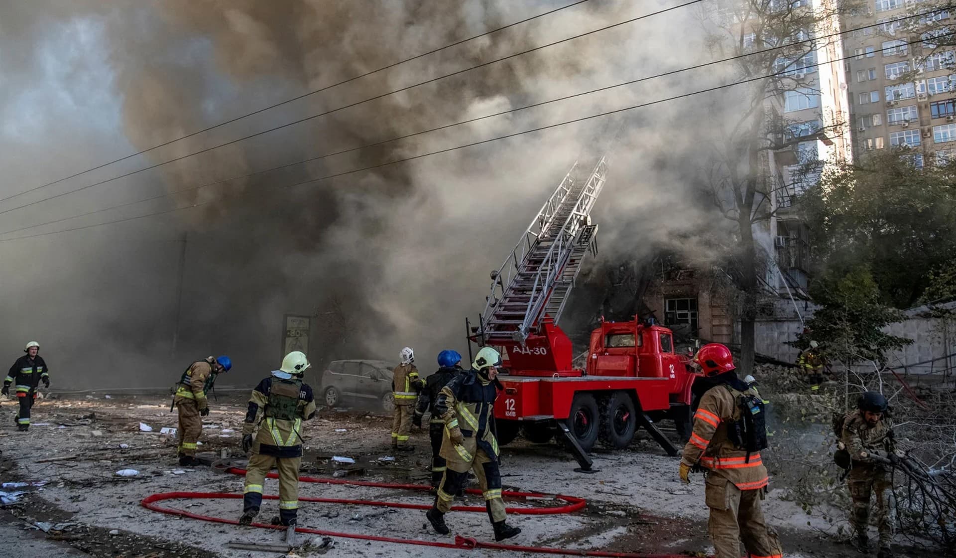 Firefighters help a local woman evacuate from a residential building destroyed in a strike by Russian drones in Kyiv