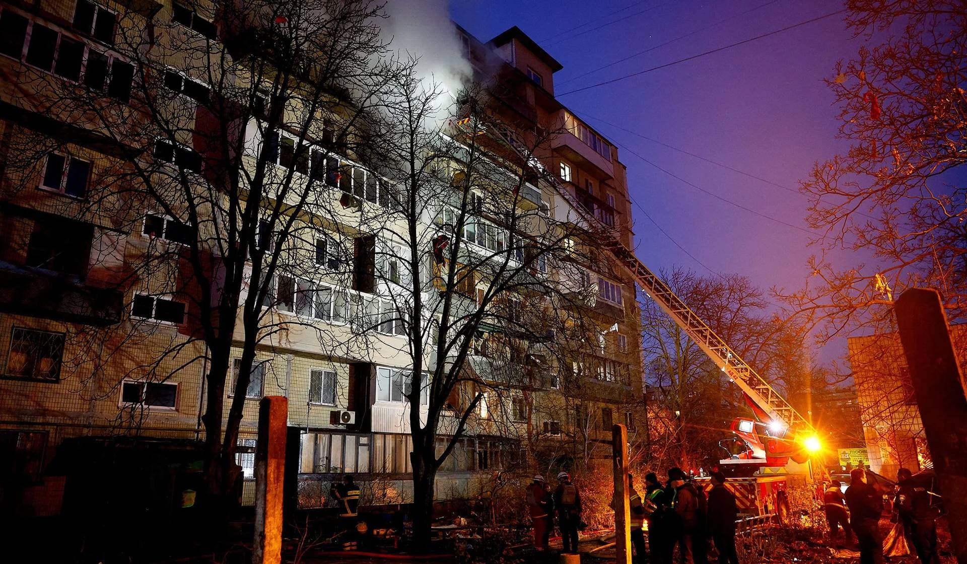 People stand as firefighters work at the site of an apartment building hit during an overnight Russian drone and missile strike in Kyiv