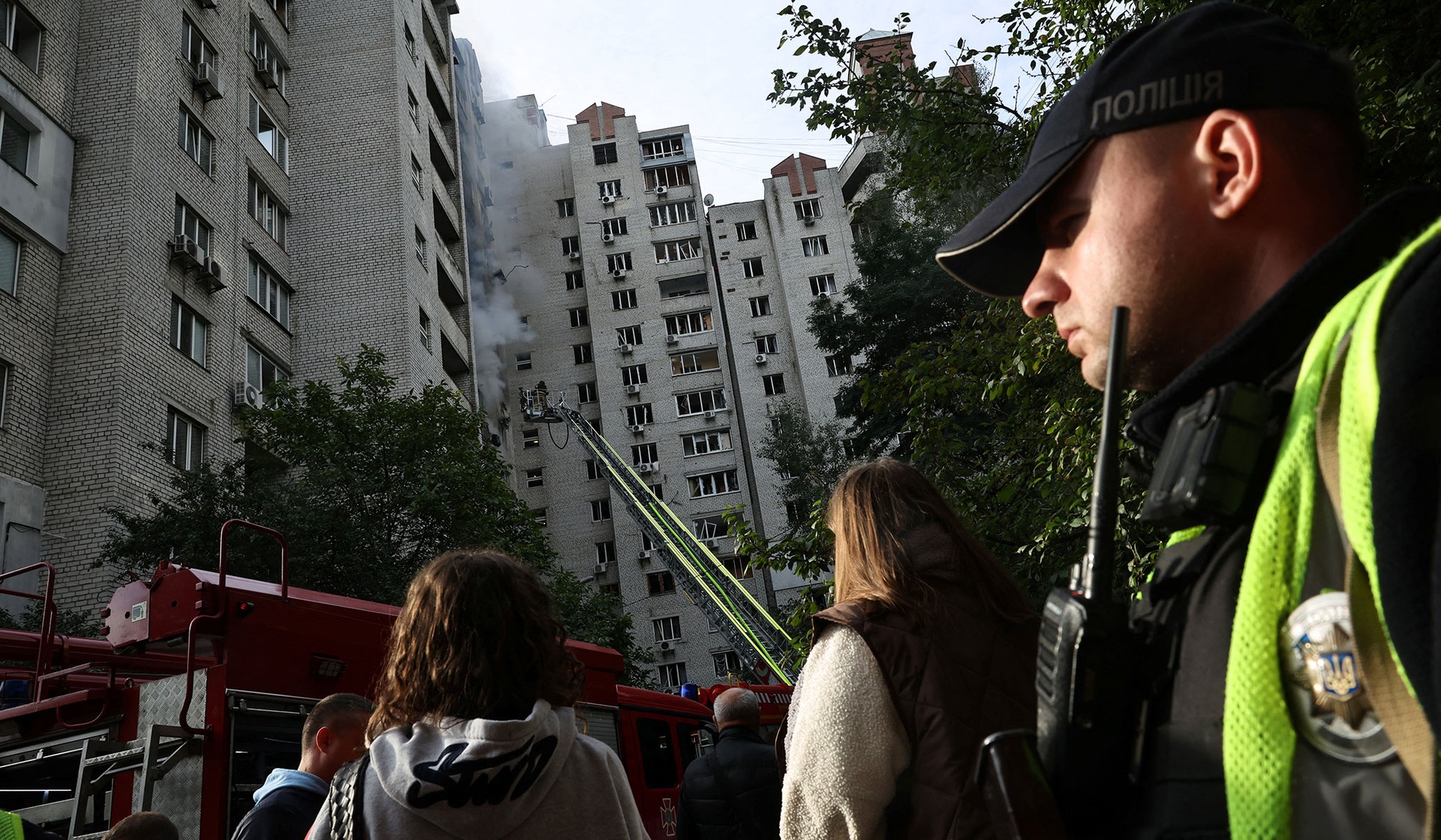 People gather as emergency personnel work at the site of an apartment building which was hit by a Russian jet drone strike in Kyiv