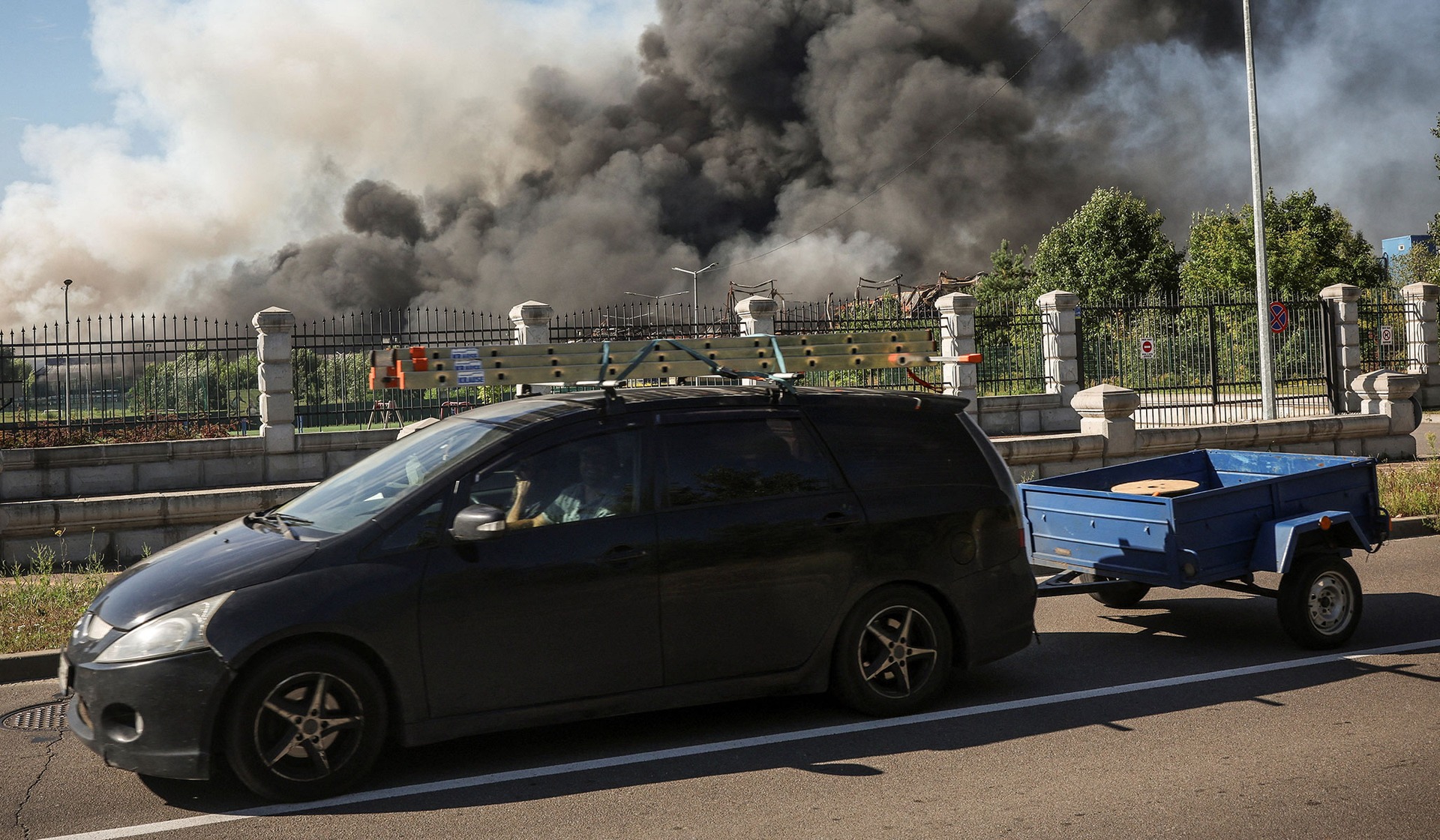 A car passes by a site of an a Russian drone strike as smoke rises in Kyiv Region