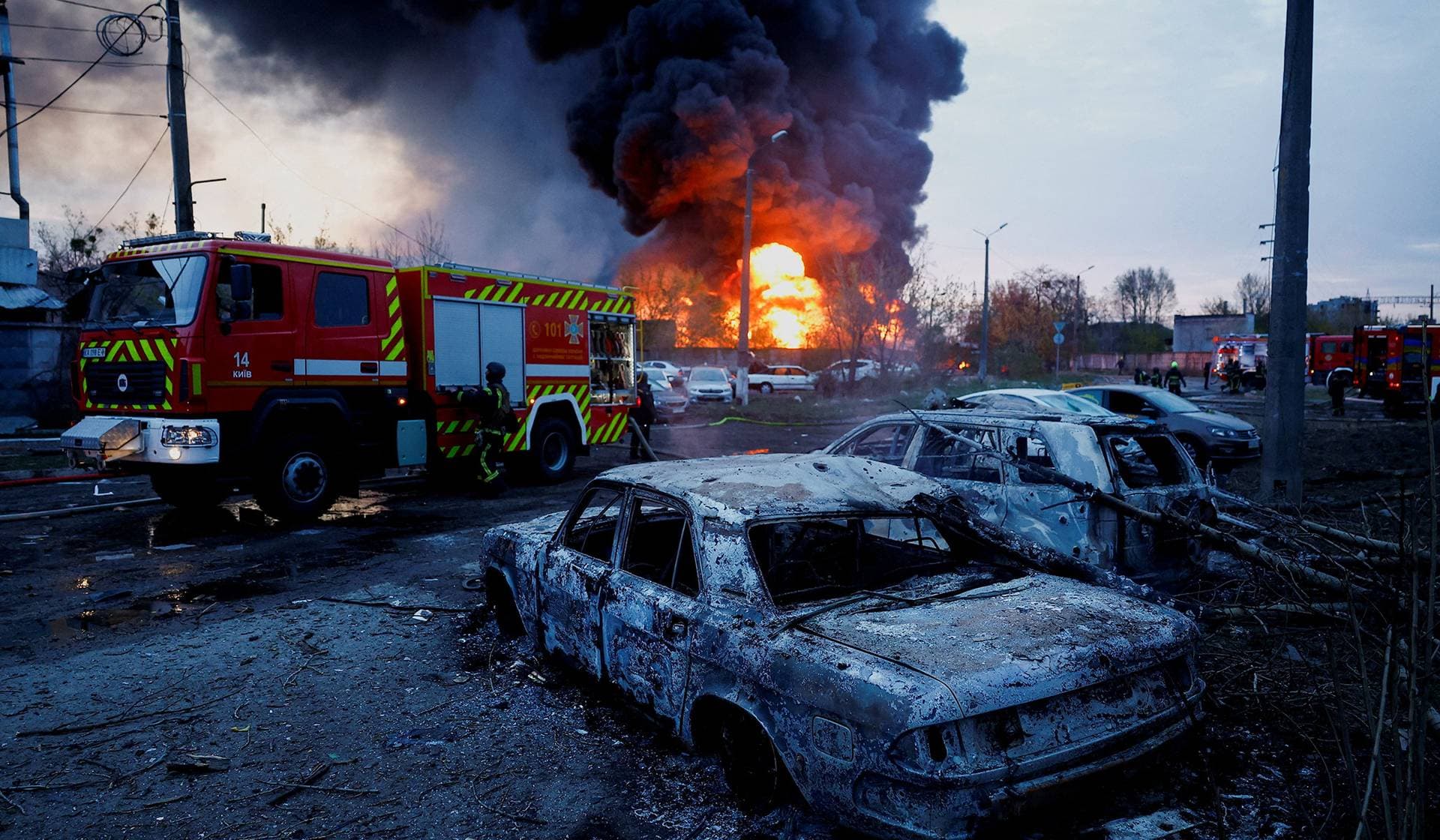 Firefighters work next to destroyed vehicles at the site of a Russian missile strike in Kyiv