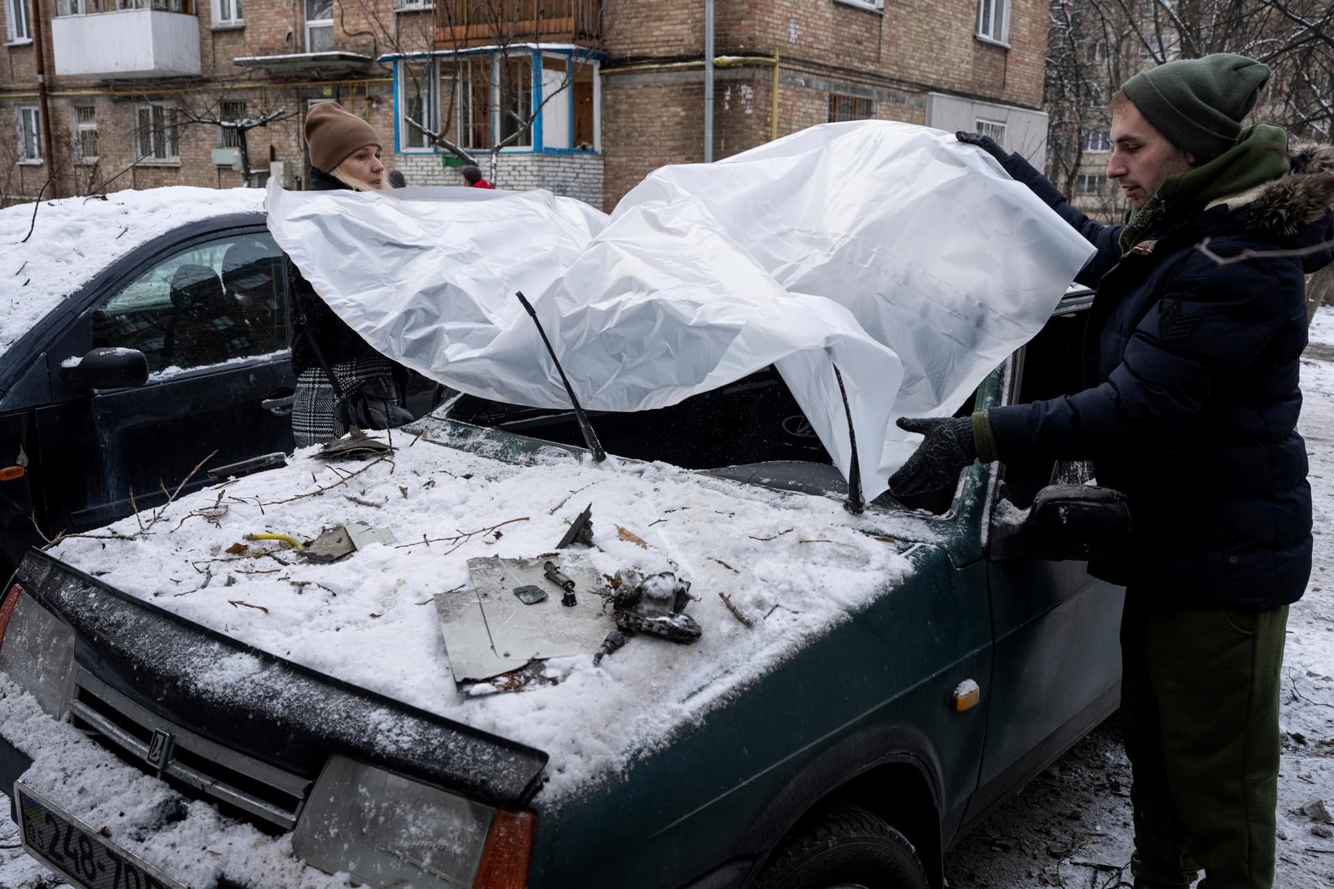 A couple cover their damaged car with a plastic tarp after a Russian attack in Kyiv