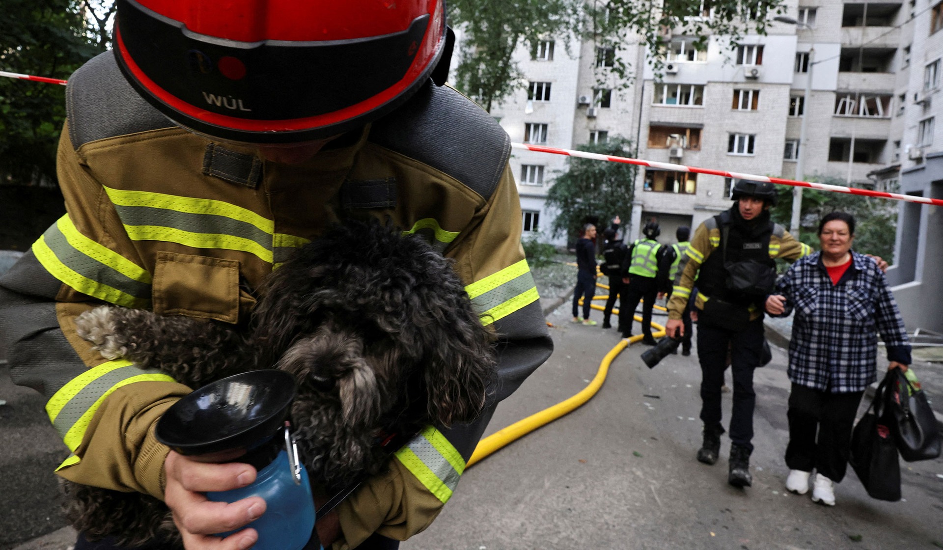 A firefighter carries a dog as a woman is evacuated at the site of an apartment building which was hit by a Russian jet drone strike in Kyiv