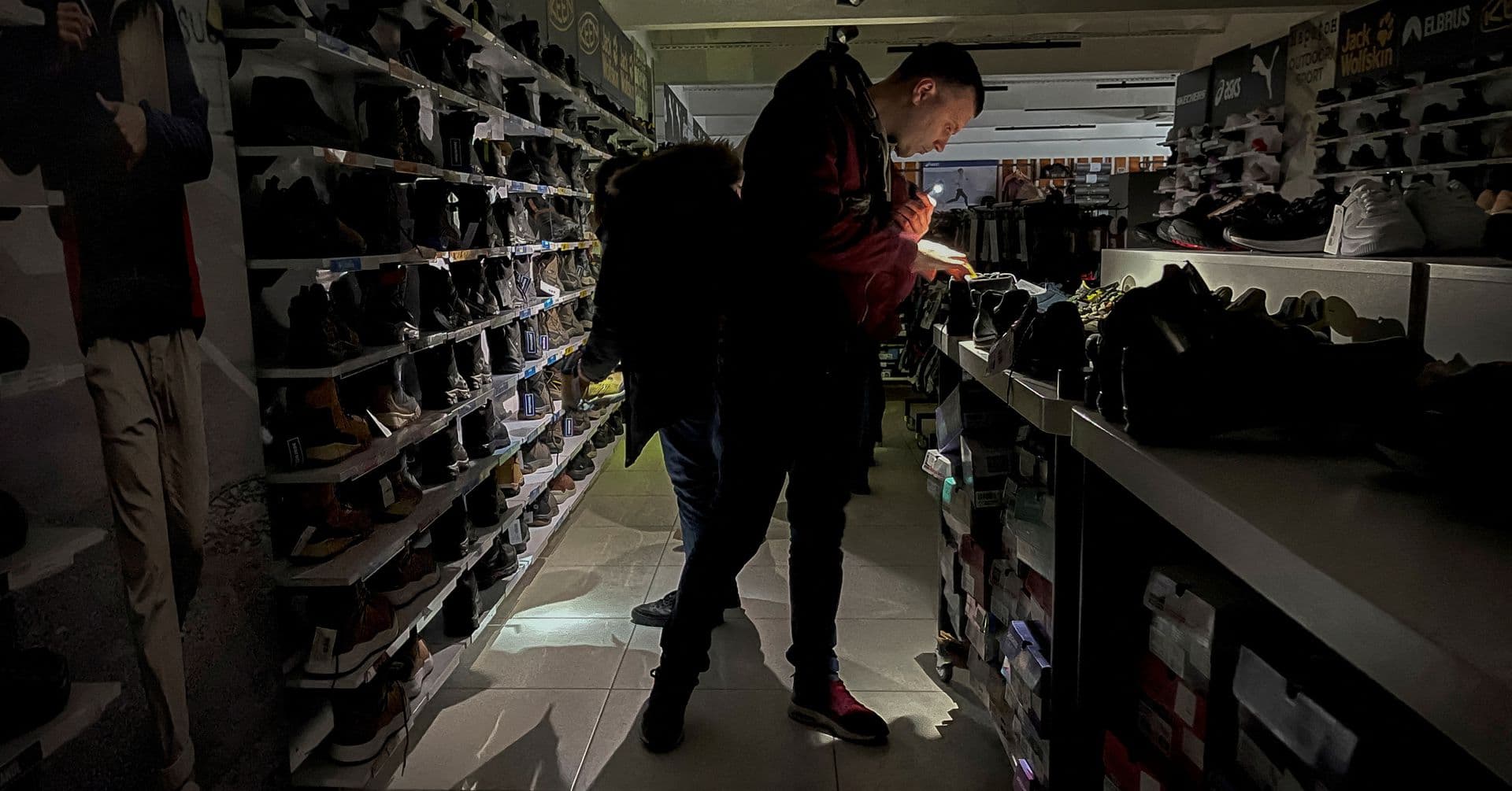 People use their mobile phone lamps to look at items at a sporting goods store during a power outage in Kyiv