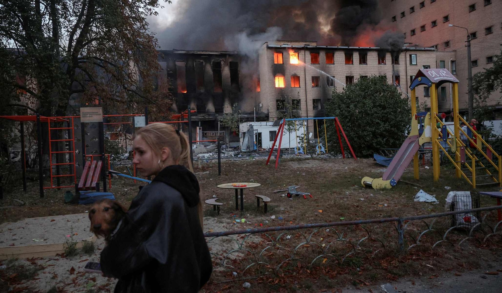 A woman carries a dog past a building hit by a Russian missile and drone strike in Kyiv