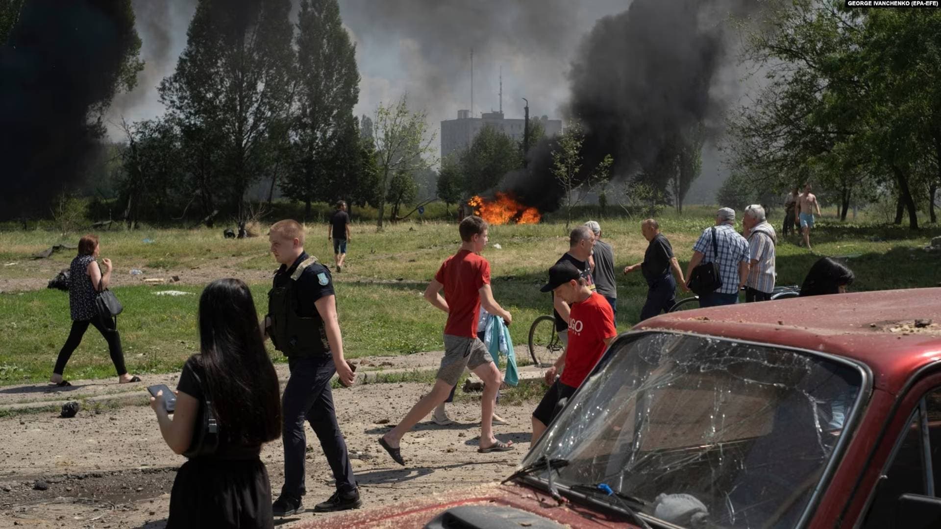 Locals react at the scene as cars burn nearby