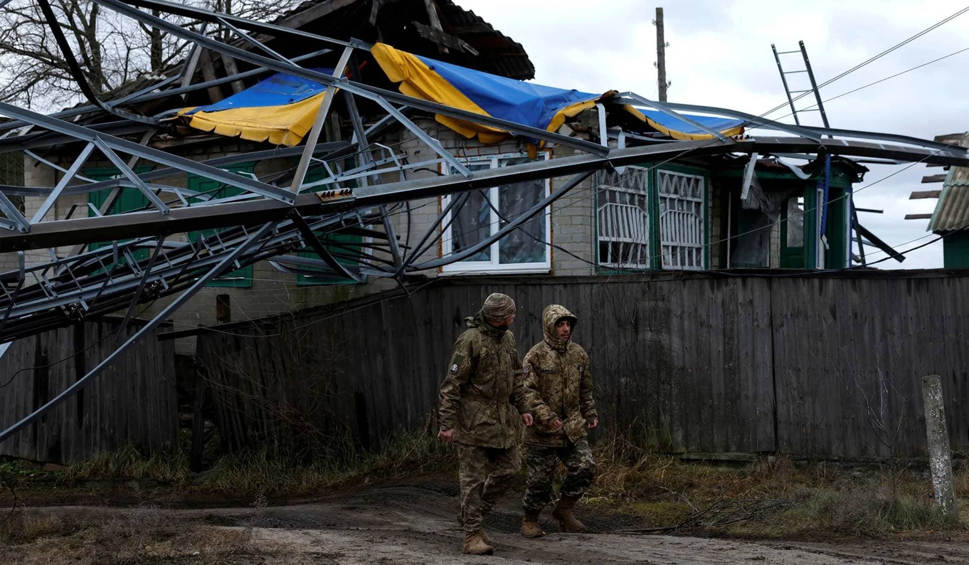 Ukrainian soldiers walk under a communications tower that fell from a strike during intense shelling in Yampil