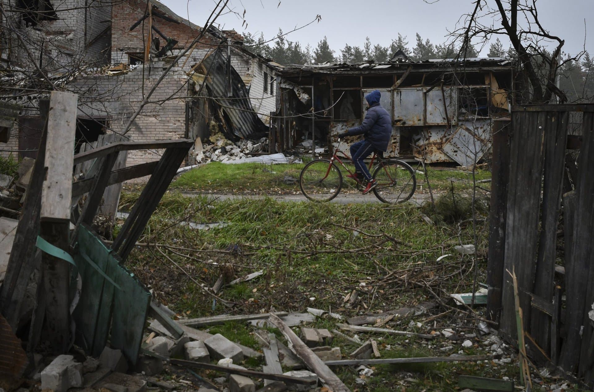 A woman rides a bicycle past destroyed buildings in the recently recaptured village of Yampil