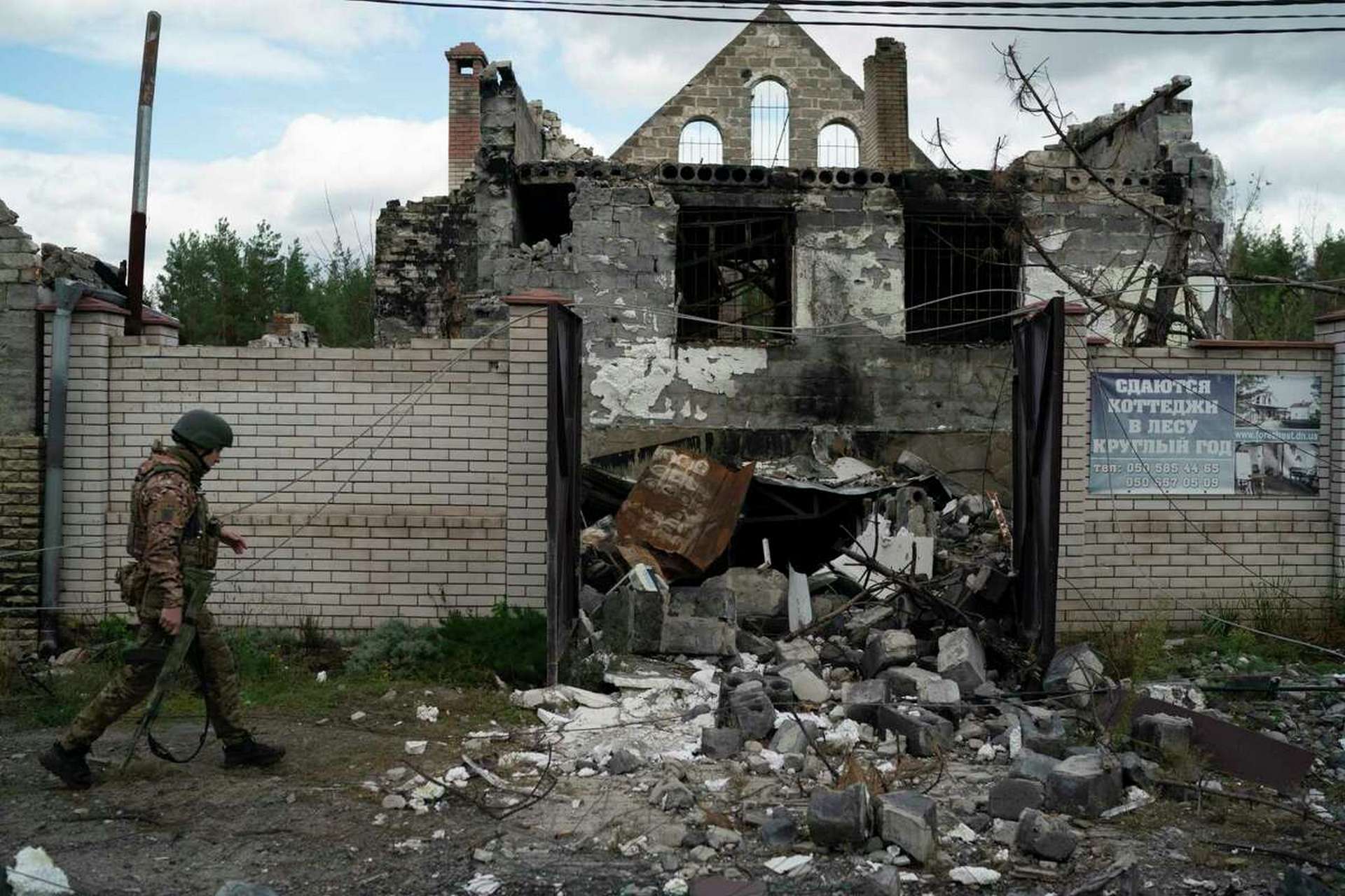 A Ukrainian serviceman walks past a damaged building in the retaken village of Shchurove
