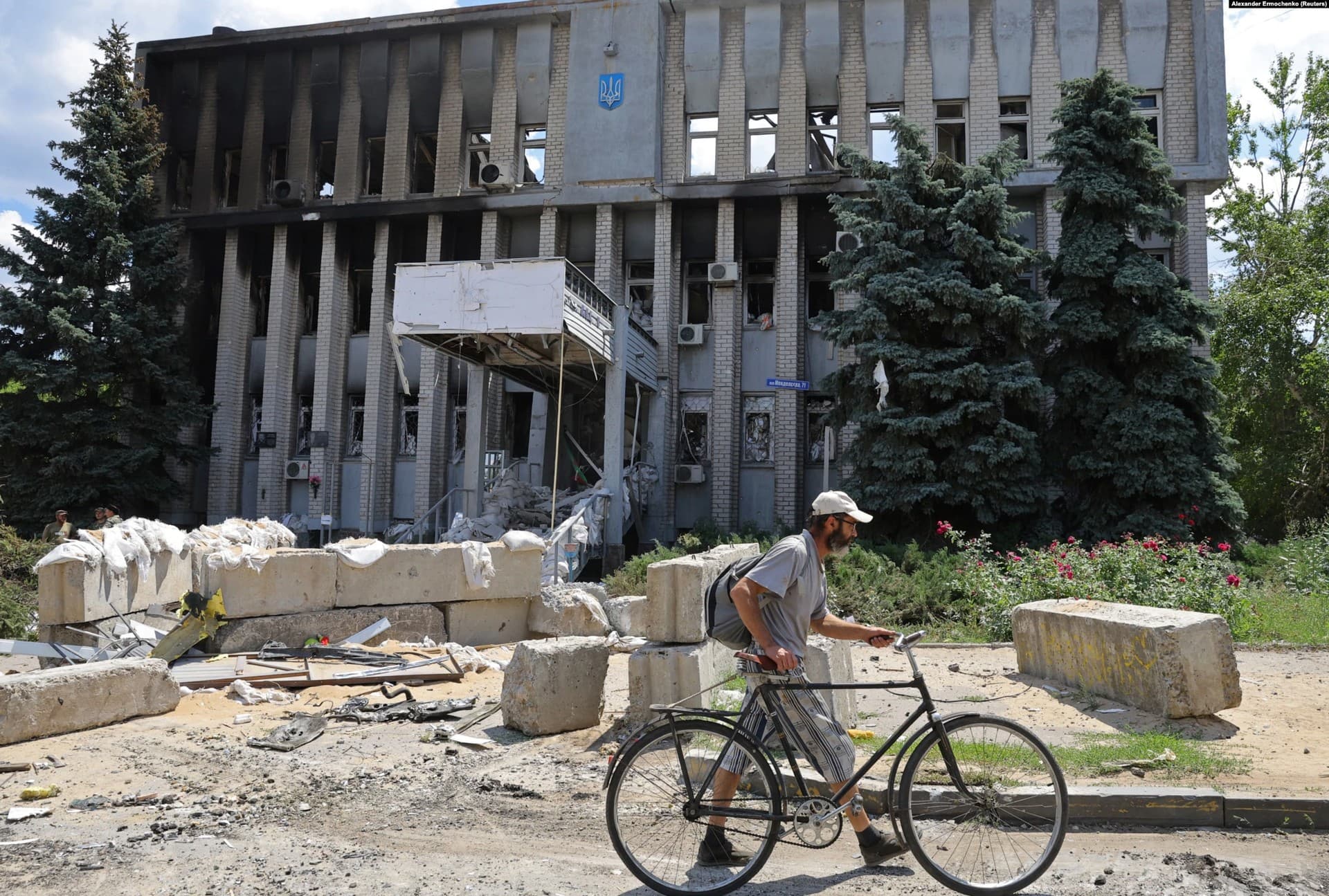 A local resident walks with a bicycle past a destroyed police department building