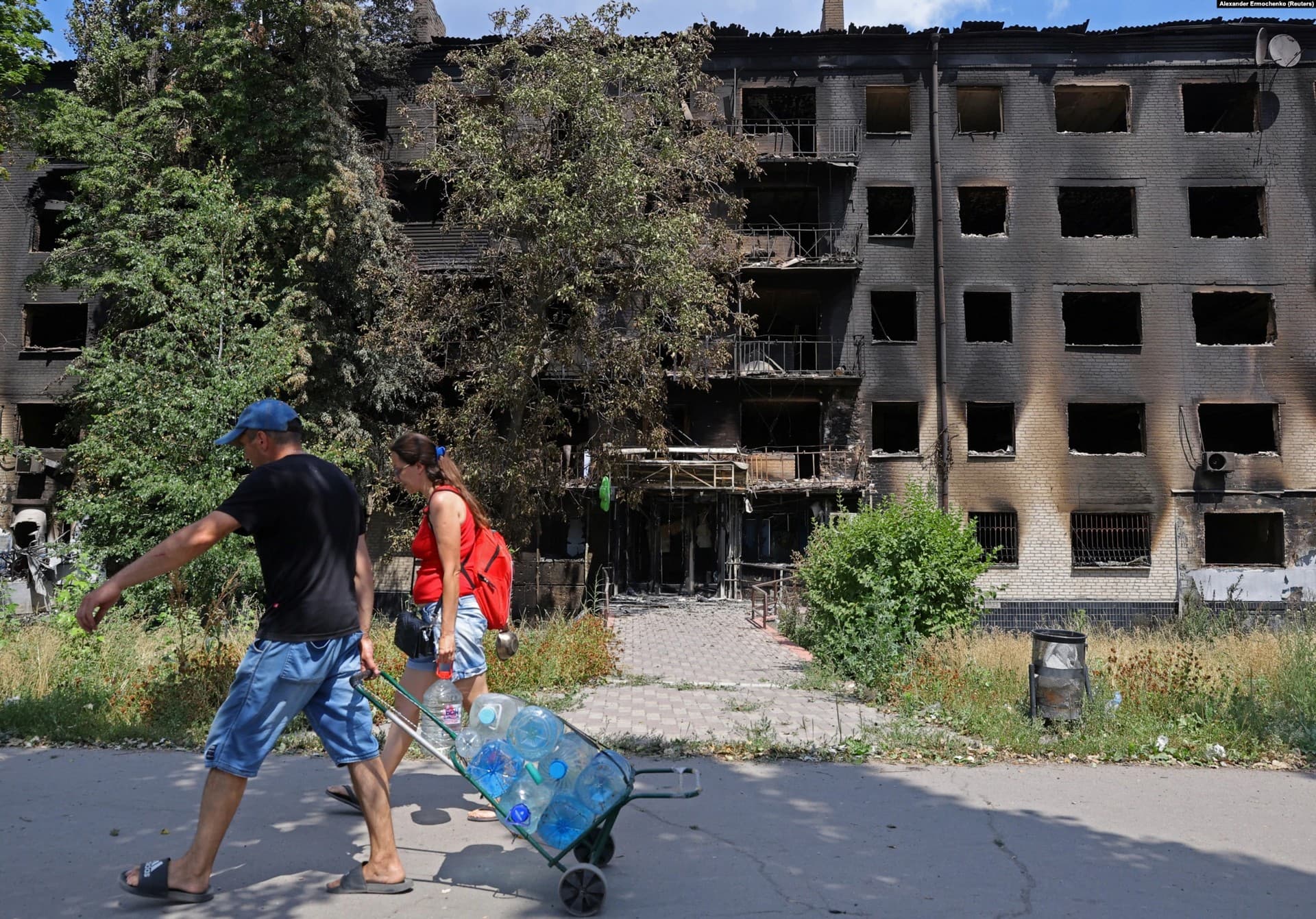 Local residents carry bottles of water past destroyed residential buildings in Lysychansk
