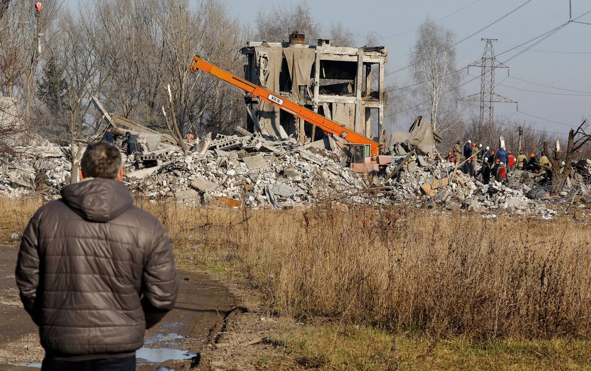 A man watches workers removing the debris of a destroyed building assumed to be a vocational college used as temporary accommodation for Russian soldiers in Makiivka