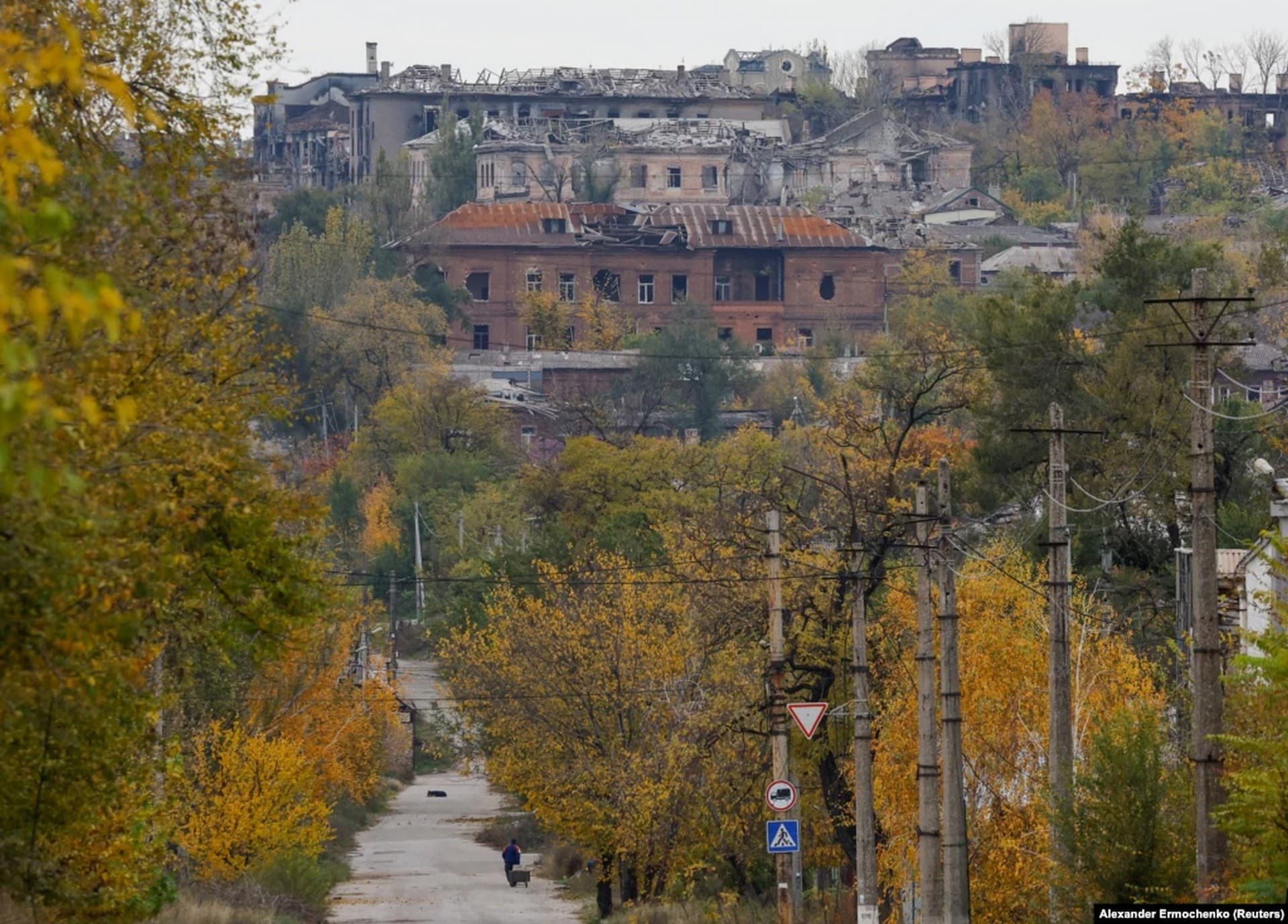 A man pulls a cart toward a destroyed suburb of Mariupol