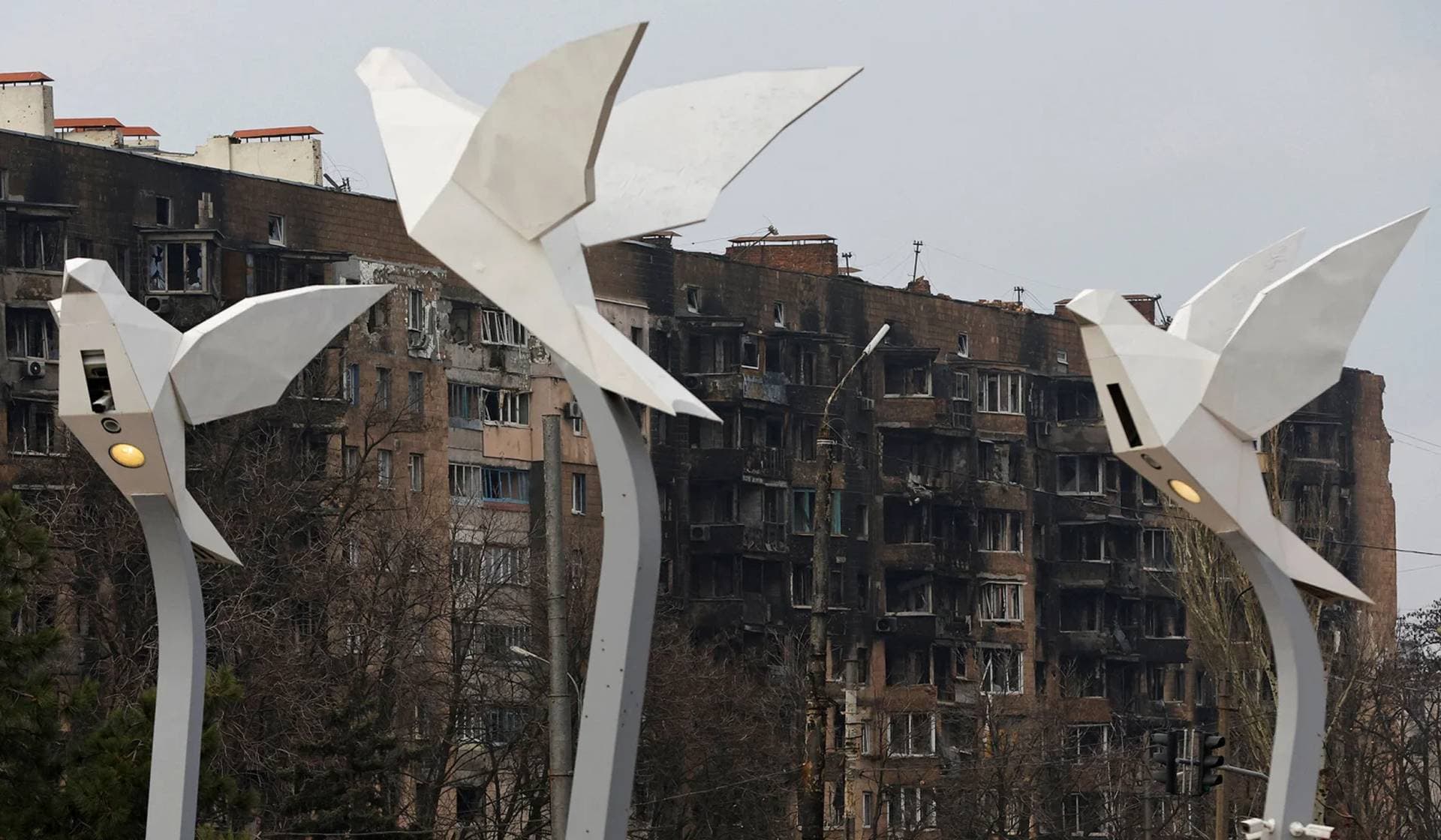 Lamp poles in the shape of doves in front of a heavily-damaged apartment building in Mariupol