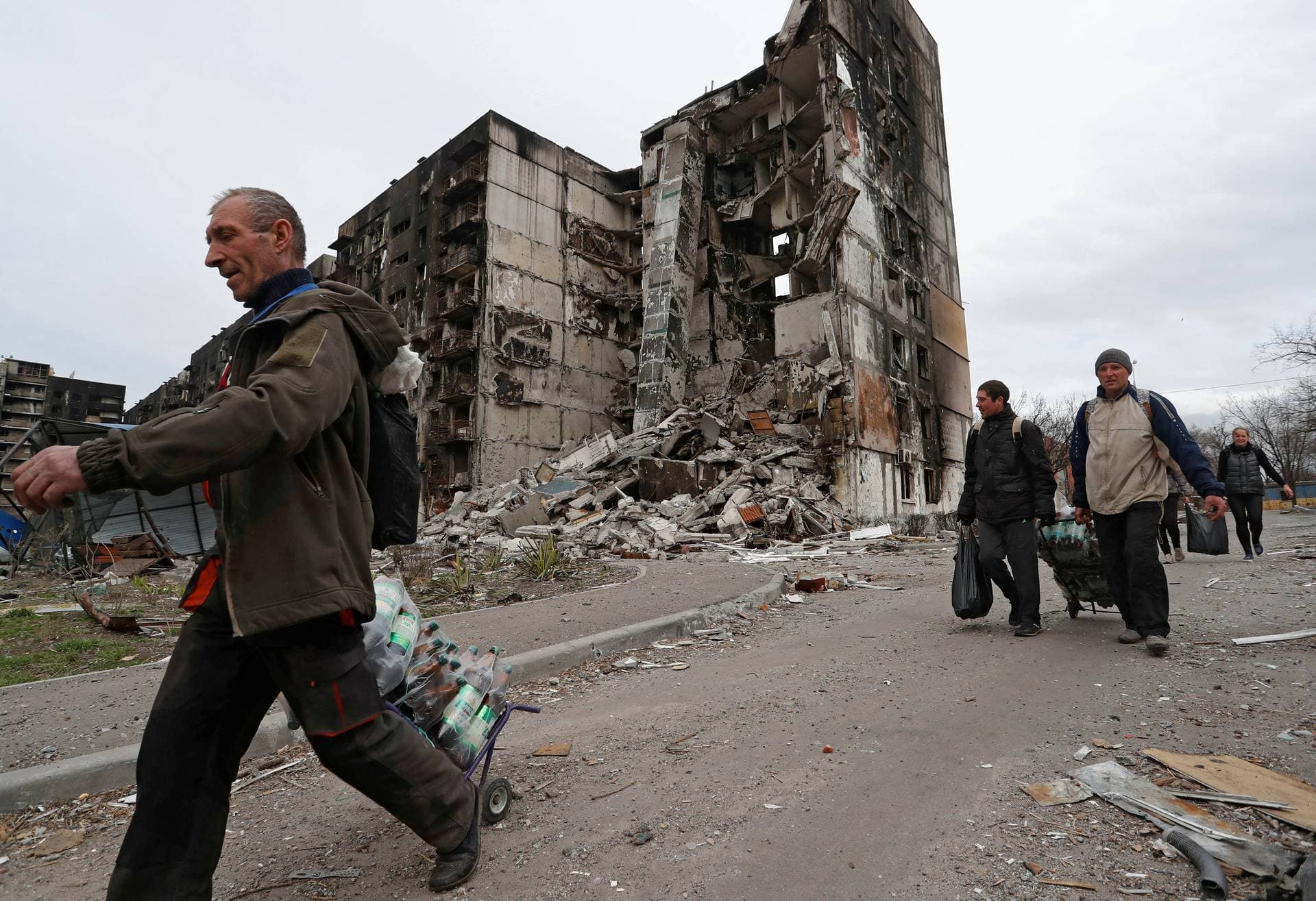 Local residents walk past a destroyed building  in Mariupol