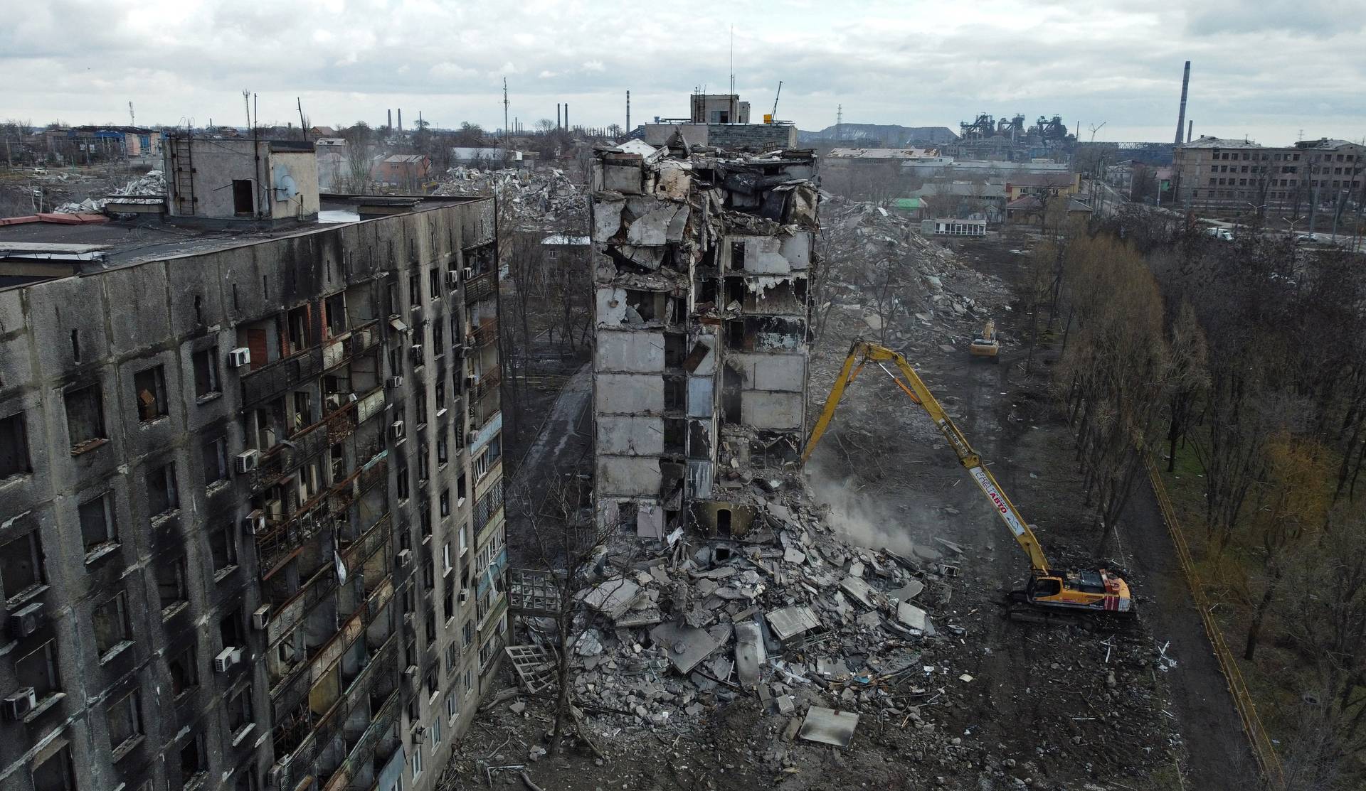An excavator demolishes a ruined apartment block in Mariupol