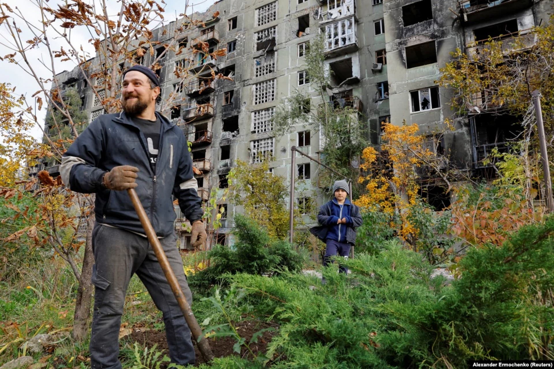 A Mariupol man and his young nephew work in the yard of a damaged building on October 29