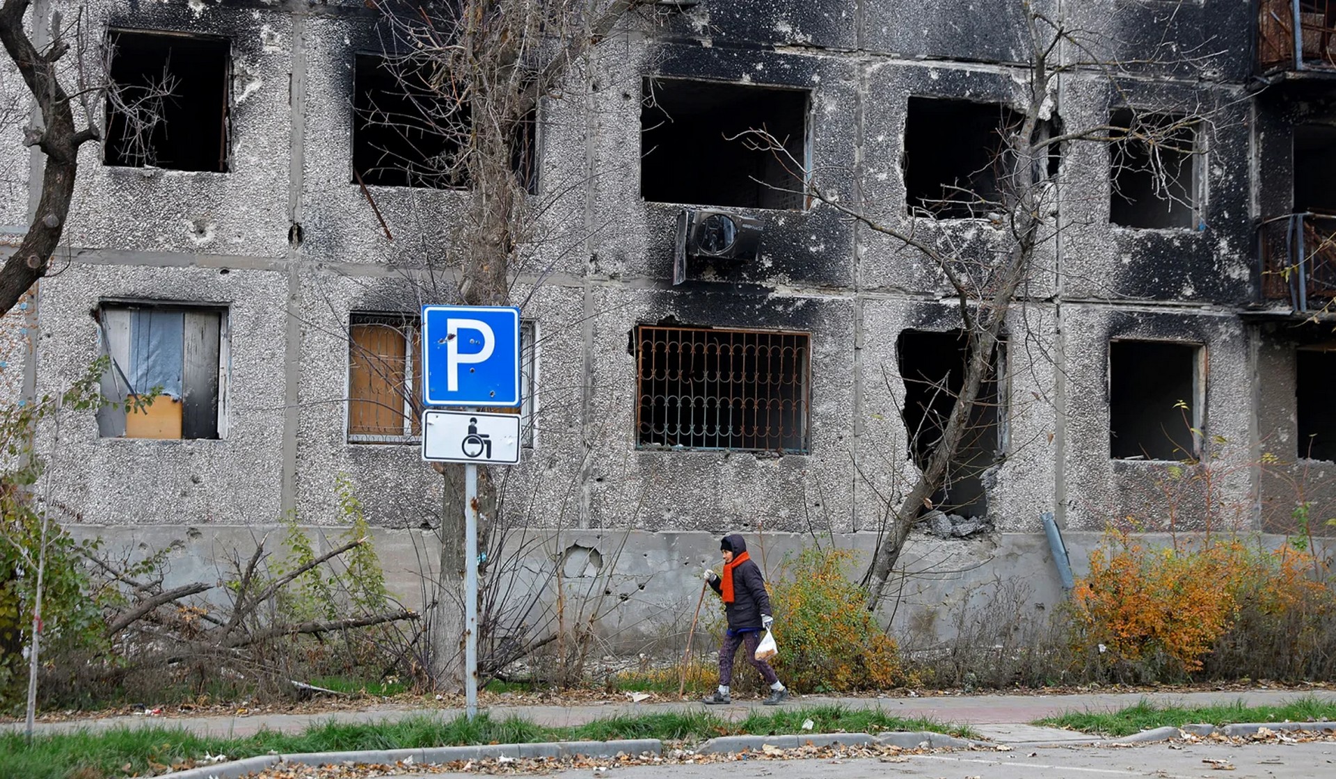 A local resident walks past a heavily damaged apartment building in Mariupol