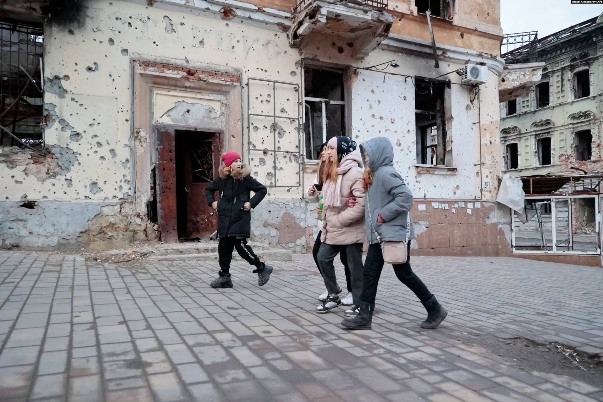 Children pass shrapnel-scarred buildings in Mariupol