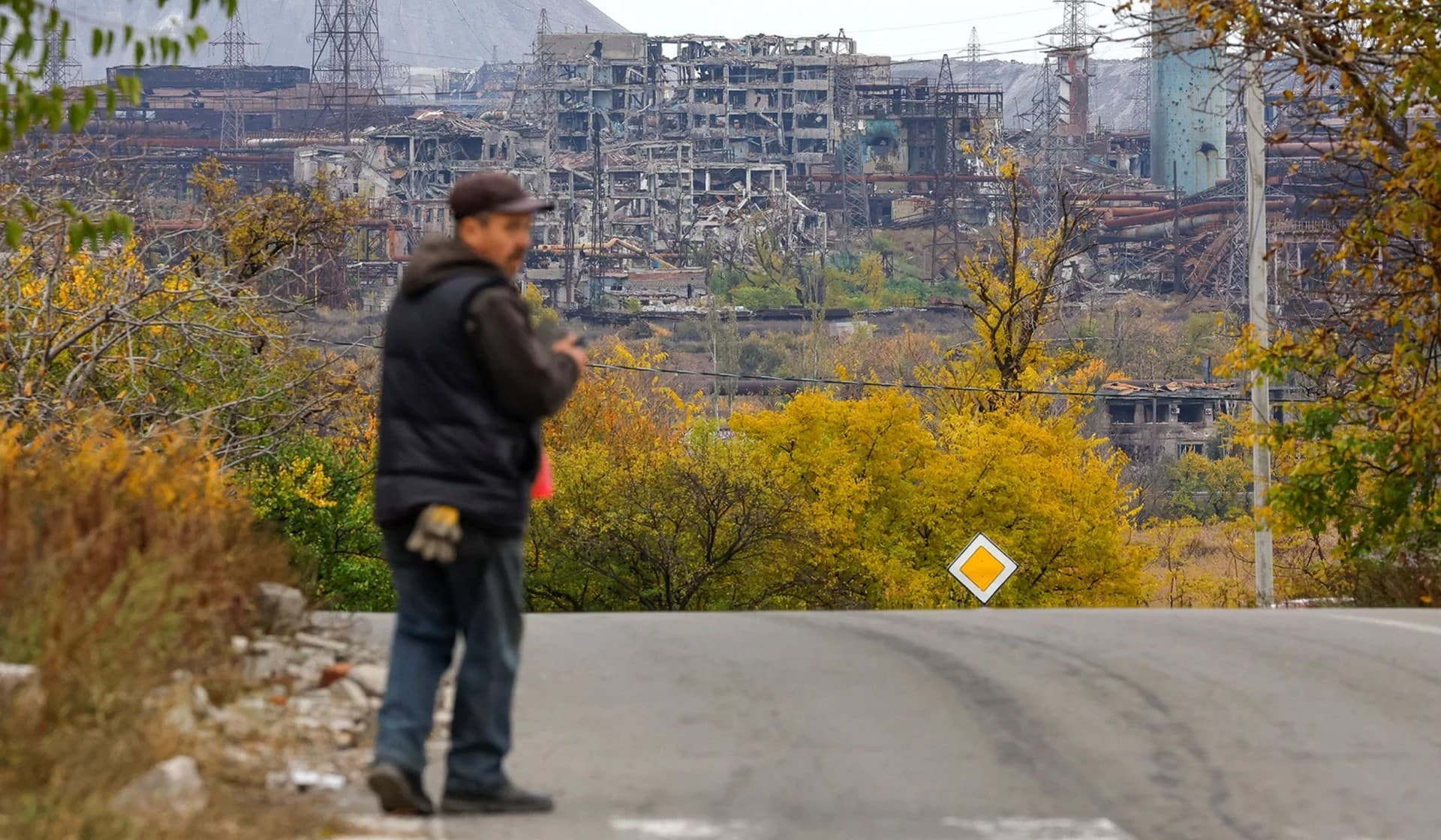 A man walks along a road with the destroyed Azovstal steel mill in the background in Mariupol