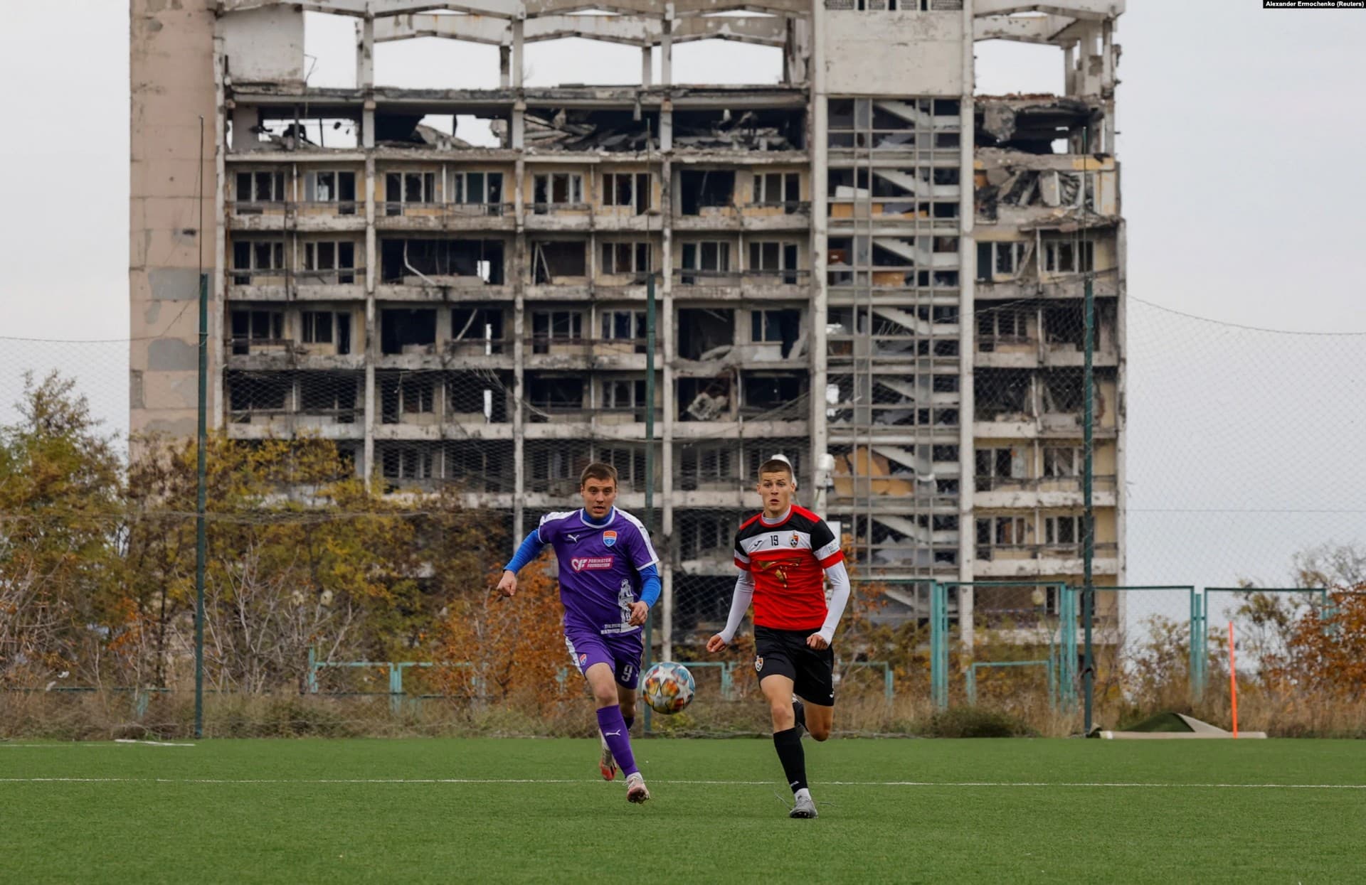 Football players train in front of a heavily damaged building