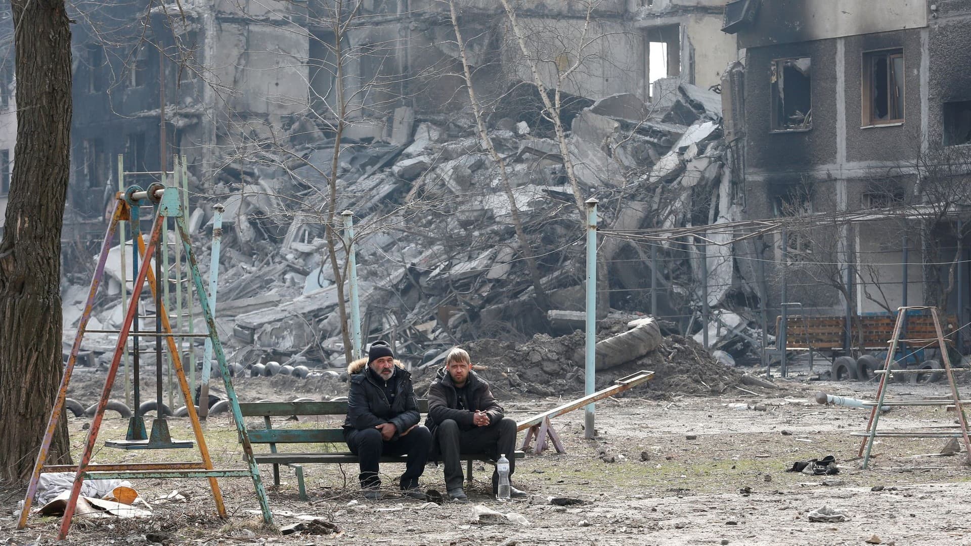 Local residents sit on a bench near an apartment building destroyed in the course of Ukraine-Russia conflict in Mariupol