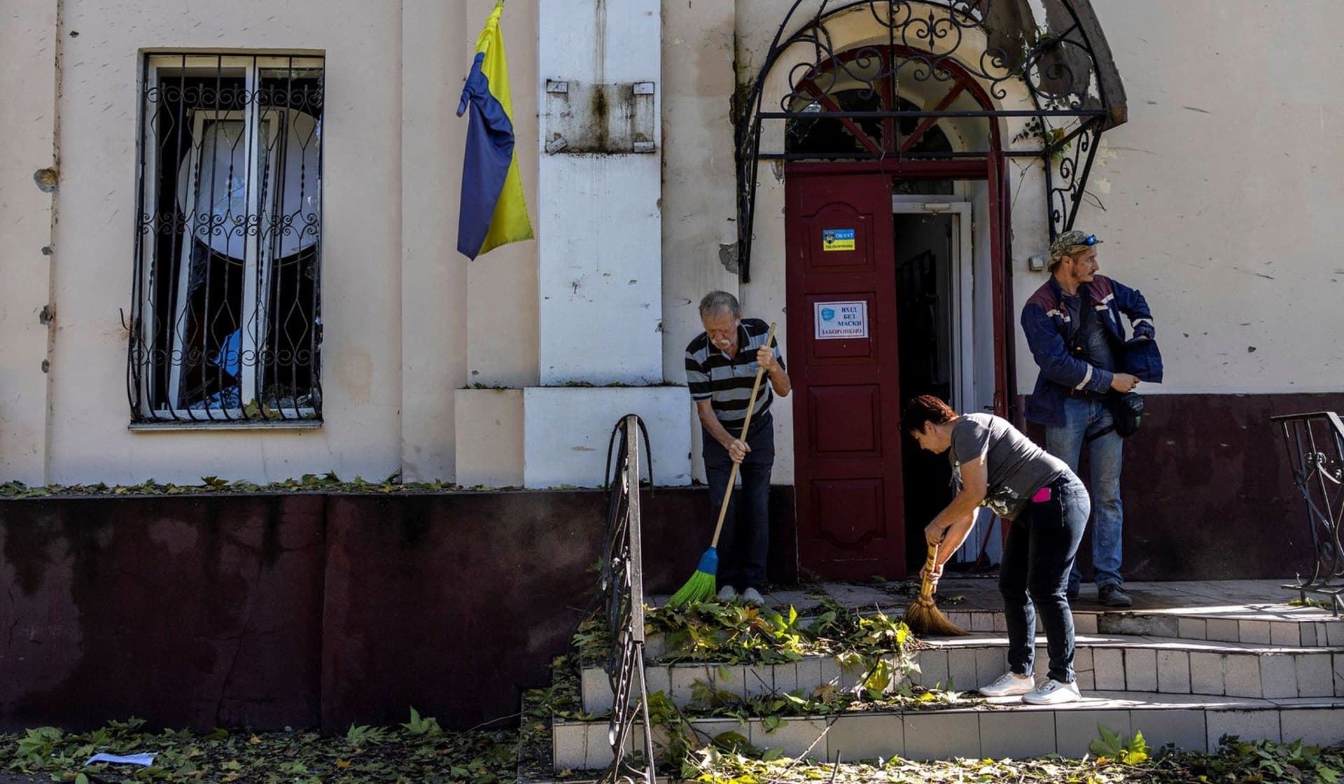People clean the entrance of a state institute destroyed by a military strike in Mykolaiv