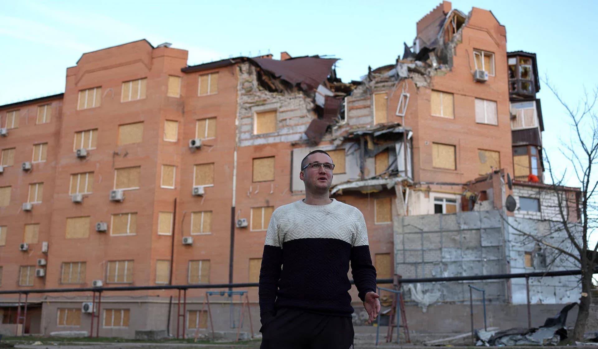 a teacher talks in front a damaged residential building in Mykolaiv