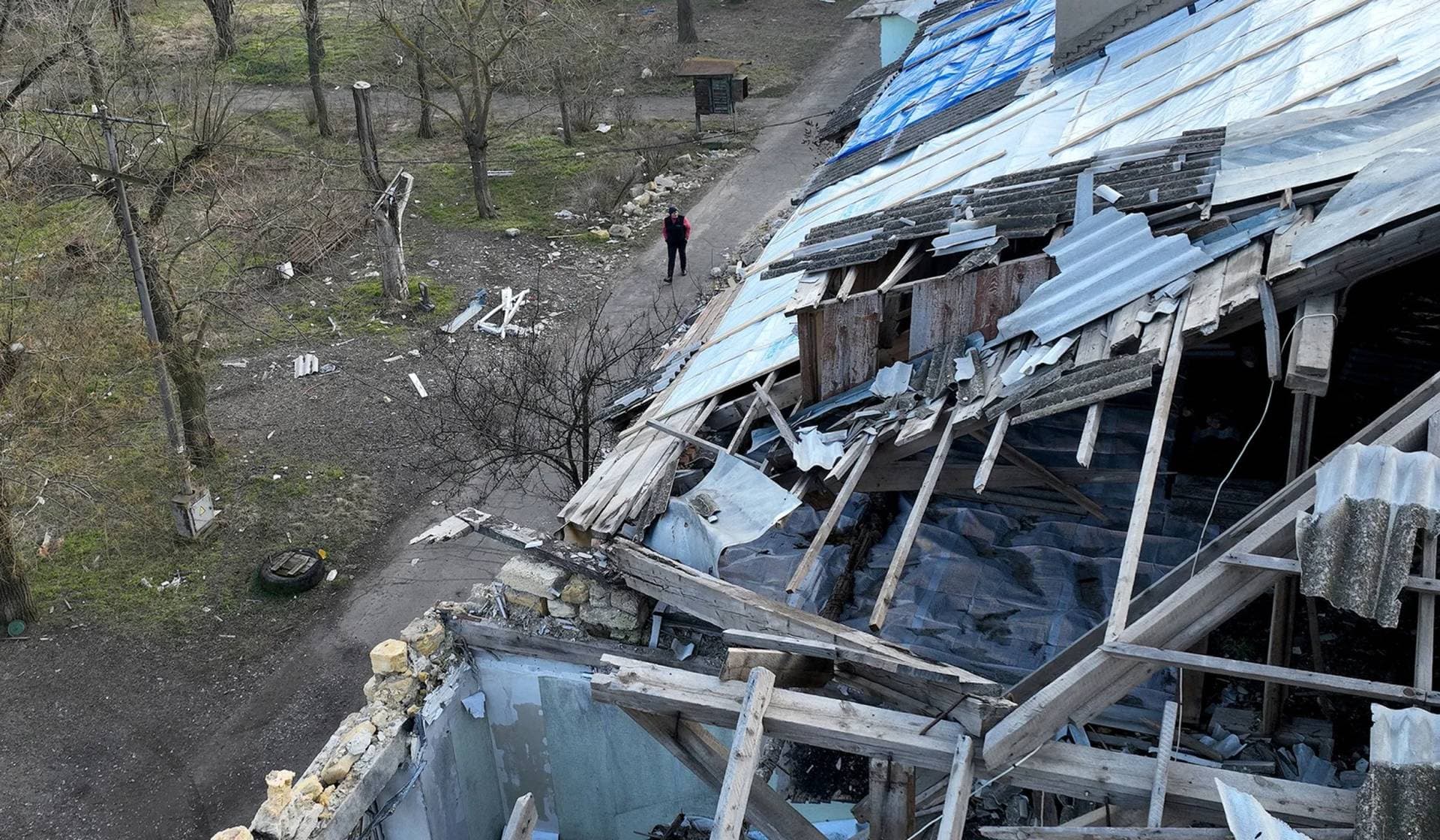 Svitlana Gynzhul walks next to a damaged house in Luch village