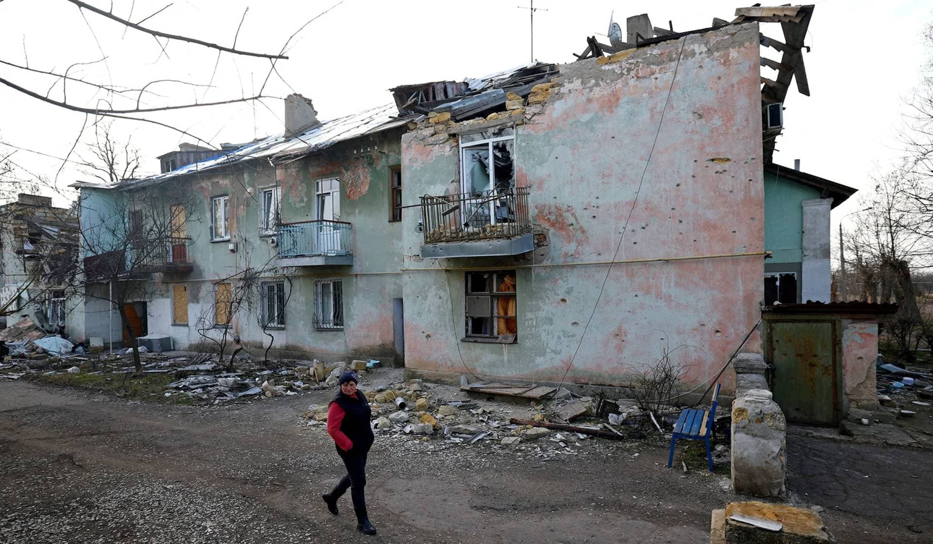 Svitlana Gynzhul walks in front of a damaged house in Luch village