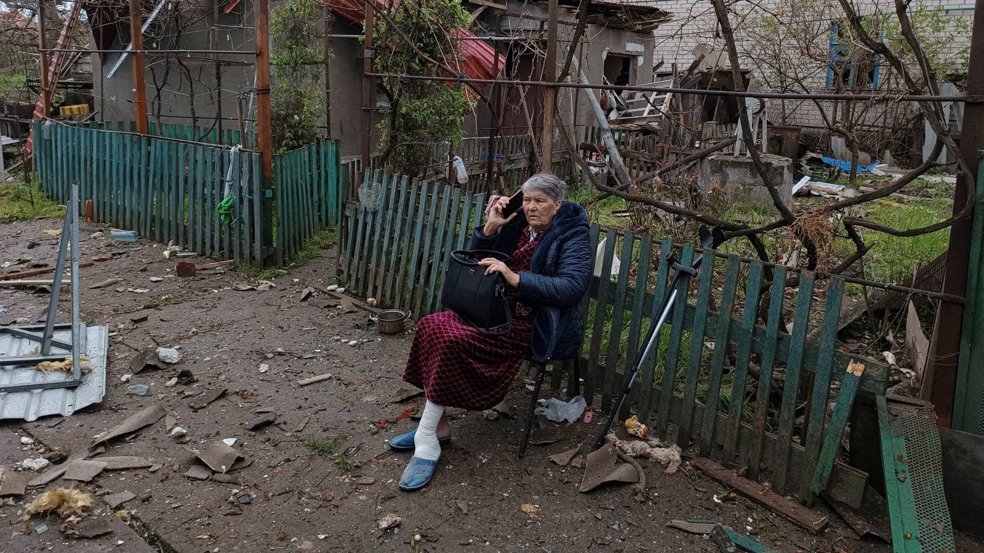 A local woman speaks on her phone as she sits on a bench next to a residential house damaged by a Russian missile strike in Mykolayiv