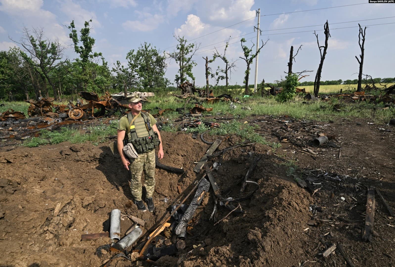 A Ukrainian soldier stands in a shell crater next to destroyed Russian military vehicles in a field near the southern city of Mykolayiv