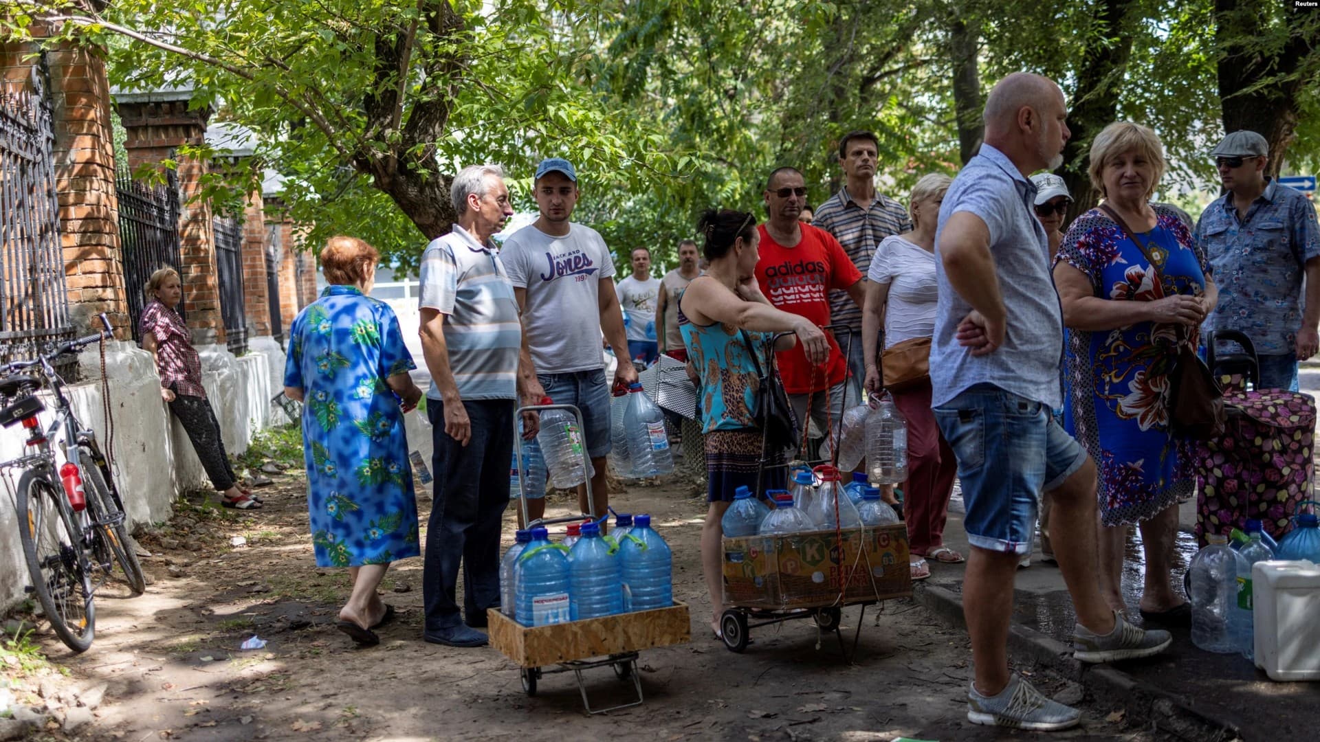 After continuous shelling that damaged infrastructure, residents of the town of Mykolayiv fill plastic bottles and jerrycans with fresh drinking water as others wait in line