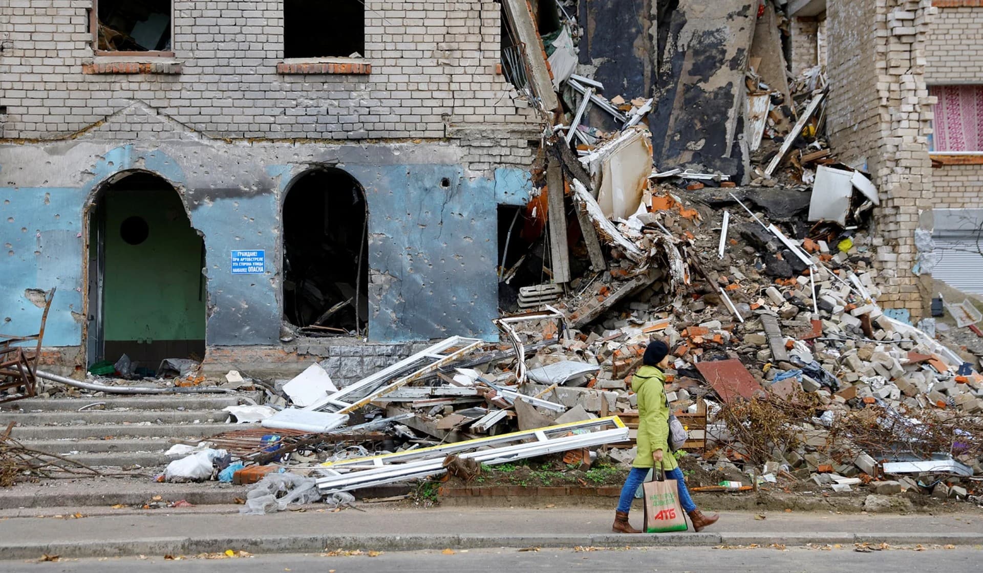 A woman walks past a damaged building Nova Kakhovka