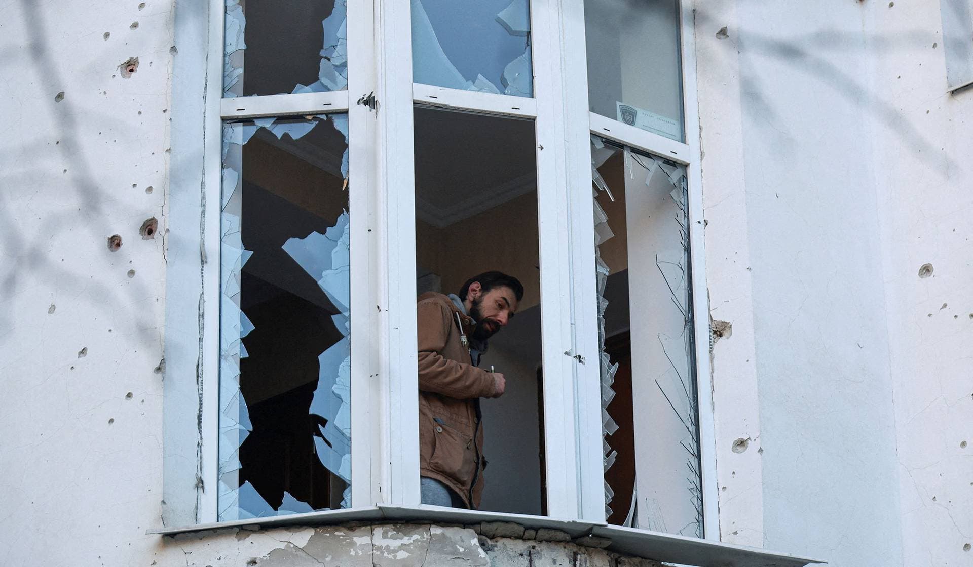 A resident looks through a broken window of his apartment damaged during Russian drone strikes in Odesa