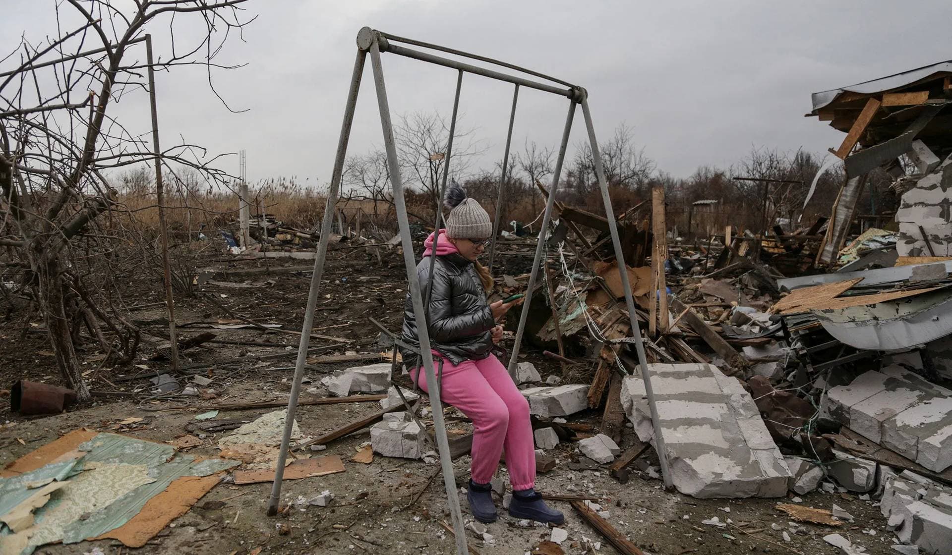 A girl uses her mobile phone while she sits on a swing at a compound of residential houses heavily damaged during a Russian drone strike in Odesa