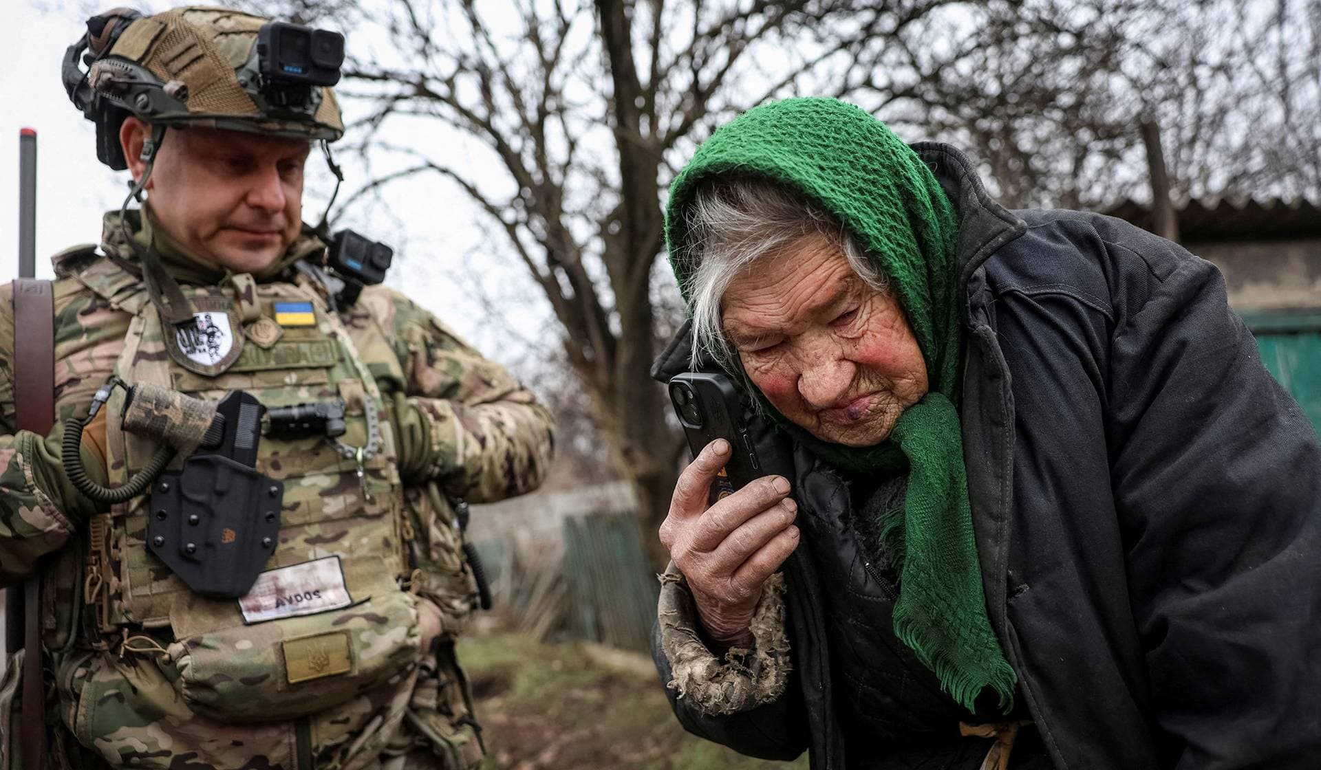 A member of the White Angels police evacuation unit stands near a resident as she speaks with her relatives during an evacuation from the frontline town of Dobropillia