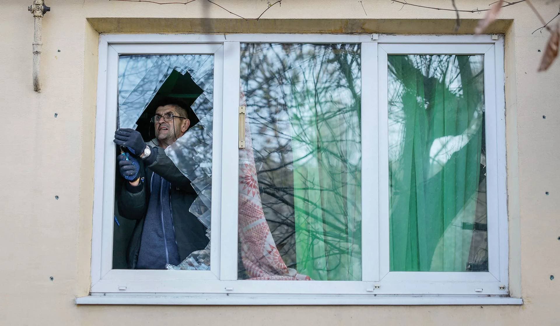 A local resident removes the broken glass from his window damaged by a Russian missile strike in Selydove