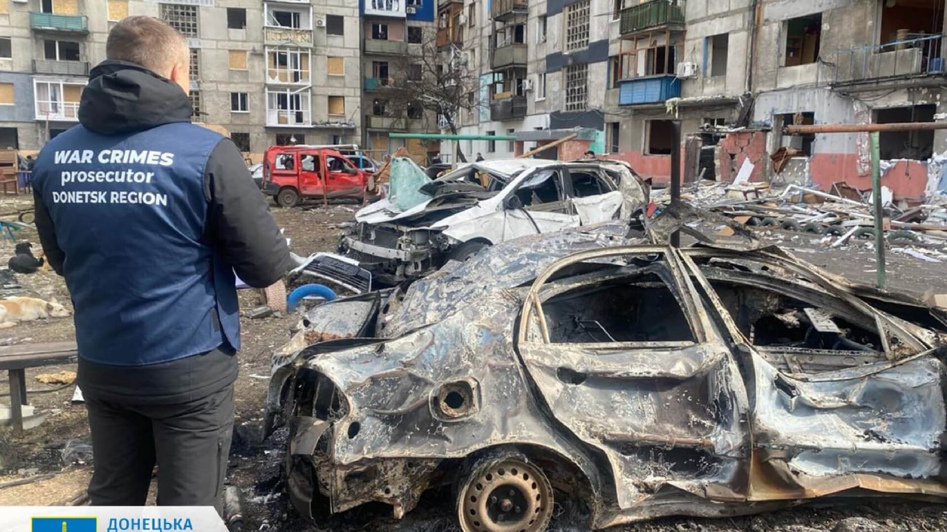 A war crimes prosecutor standing next to destroyed cars in the courtyard of a damaged residential building following a missile attack in Myrnohrad