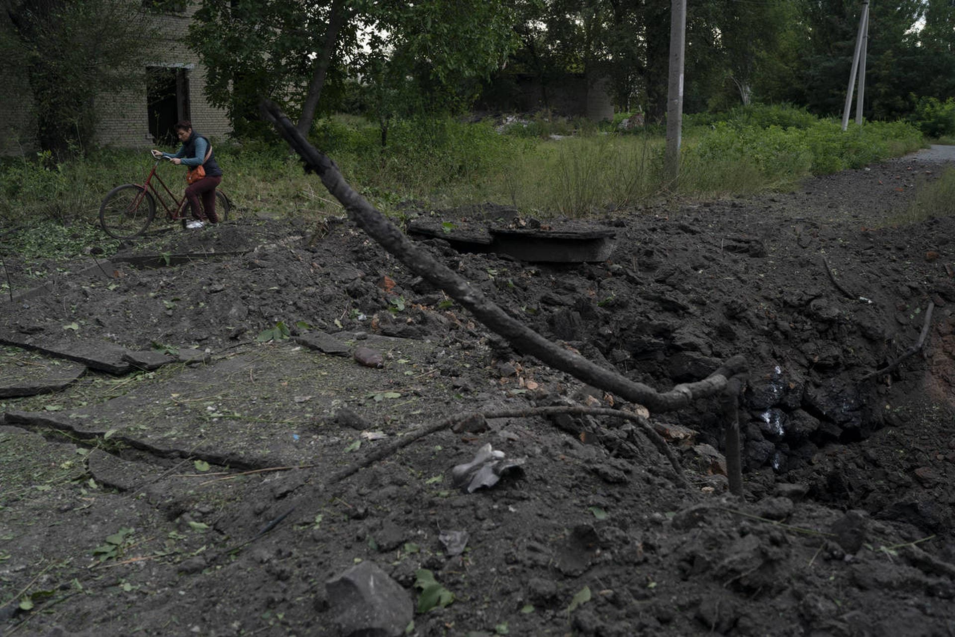 A woman walks past a crater created by an explosion after a Russian attack in Pokrovsk region
