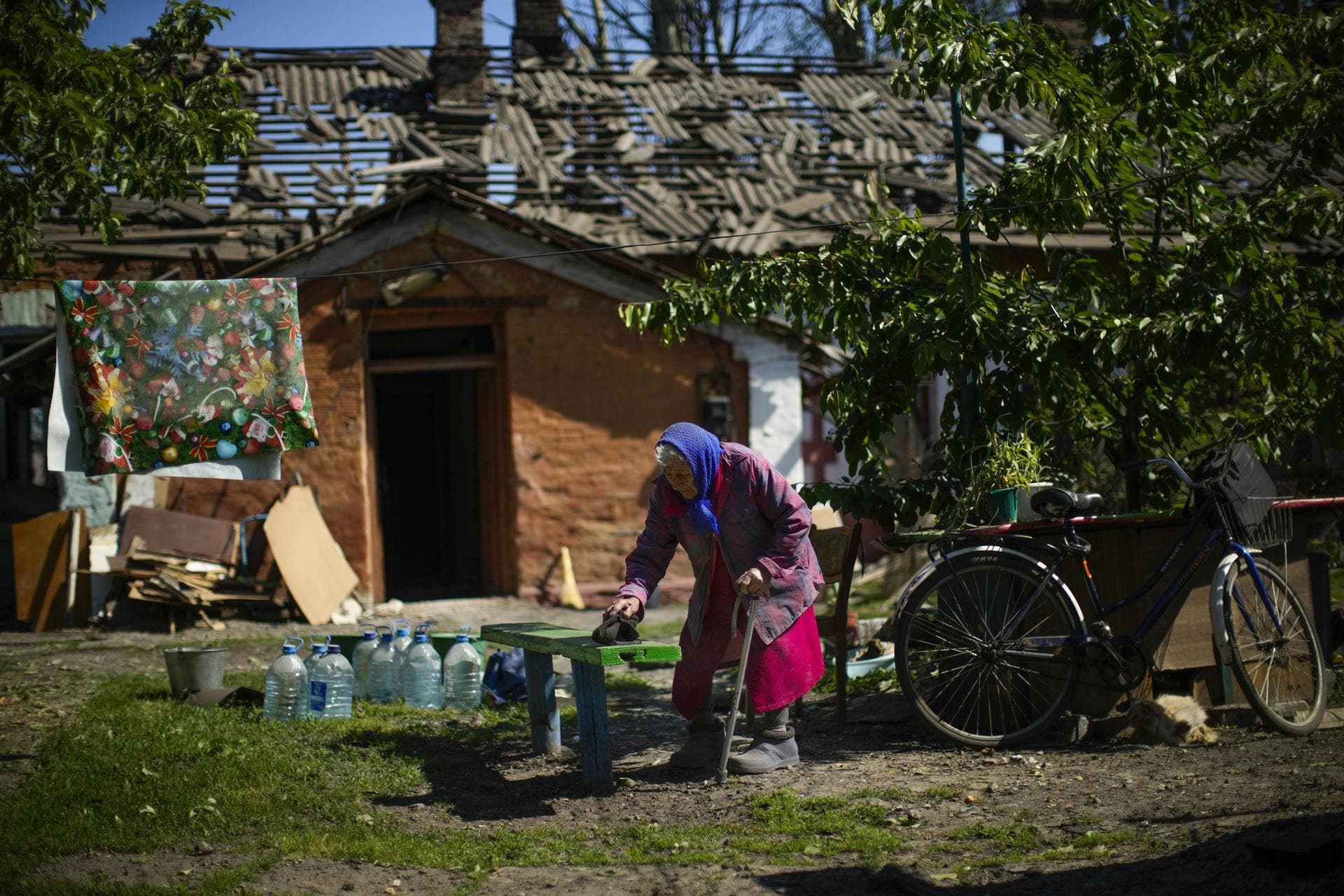 Local resident Valeria removes dust from a bench outside her heavily damaged house, background, after a Russian strike in Pokrovsk