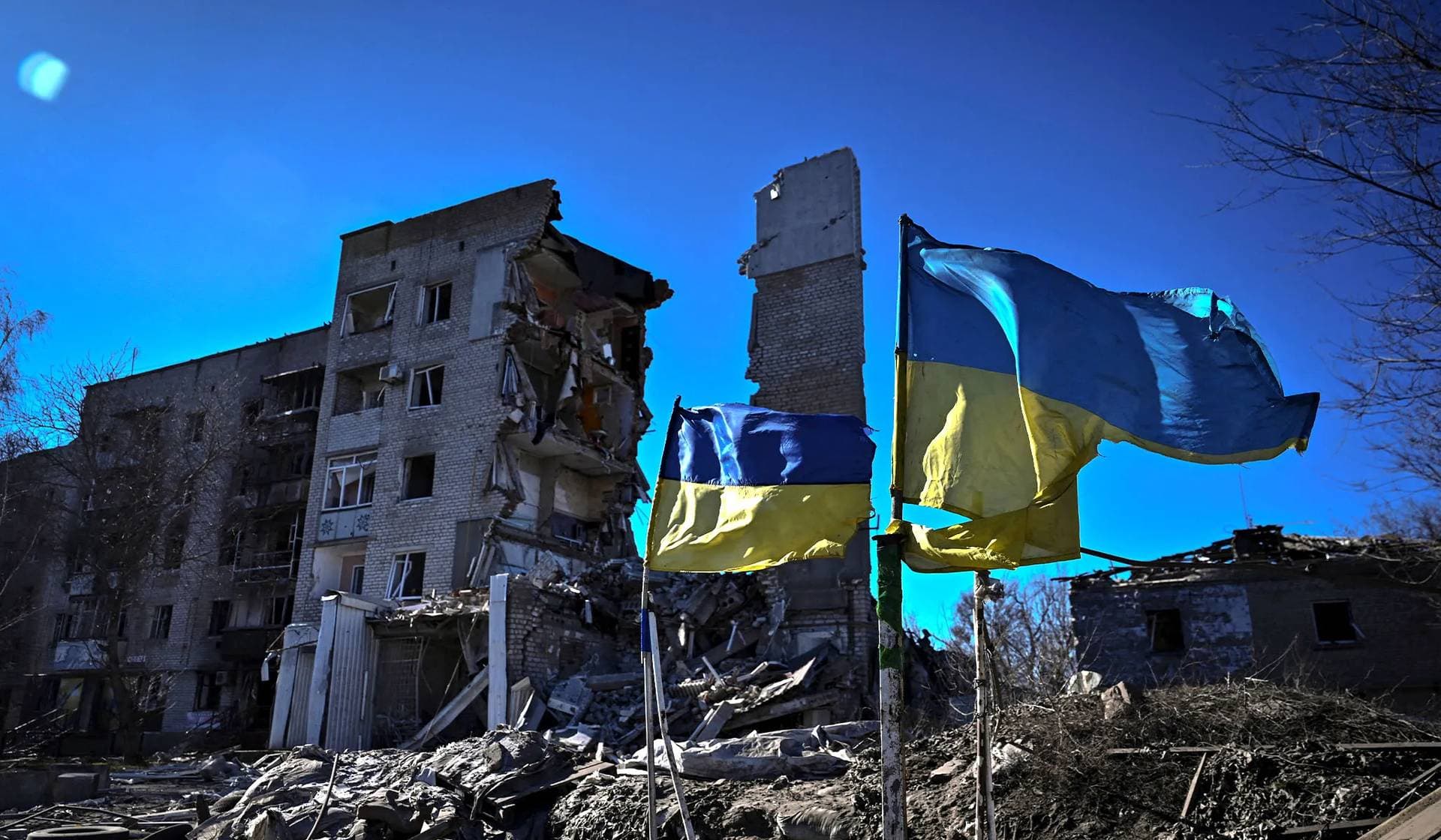 Ukrainian national flags flutter in front of a heavily damaged apartment building in Orikhiv