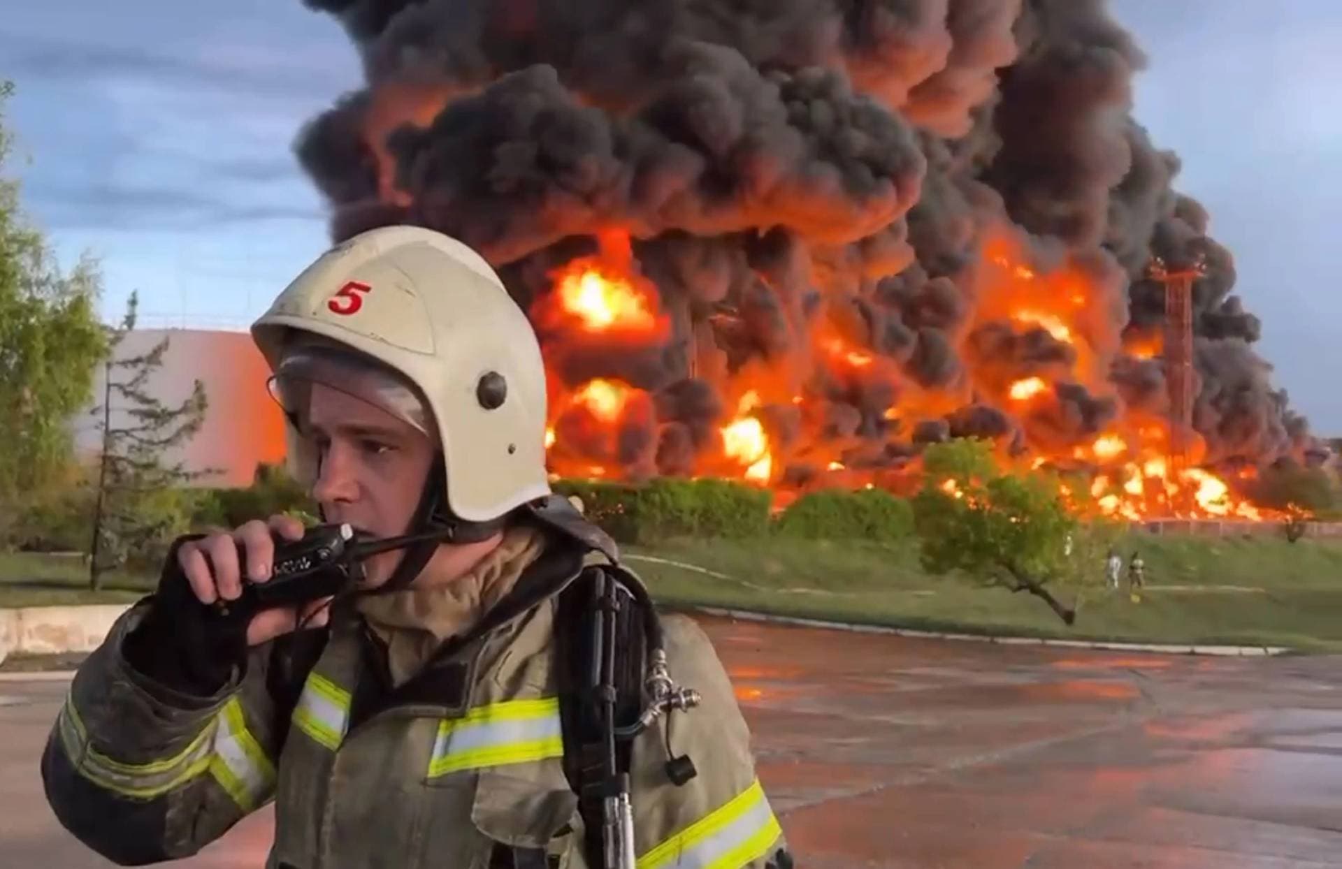 a firefighter speaks on the walkie talkie as smoke and flame rise from a burning fuel tank in Sevastopol