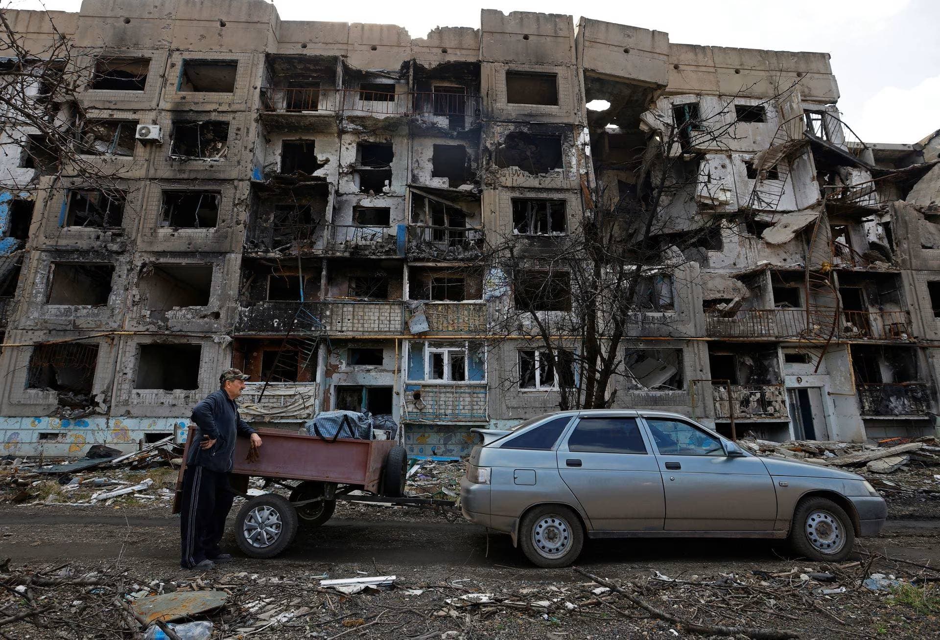 A resident stands next to a car in front of a residential building heavily damaged in the settlement of Toshkivka